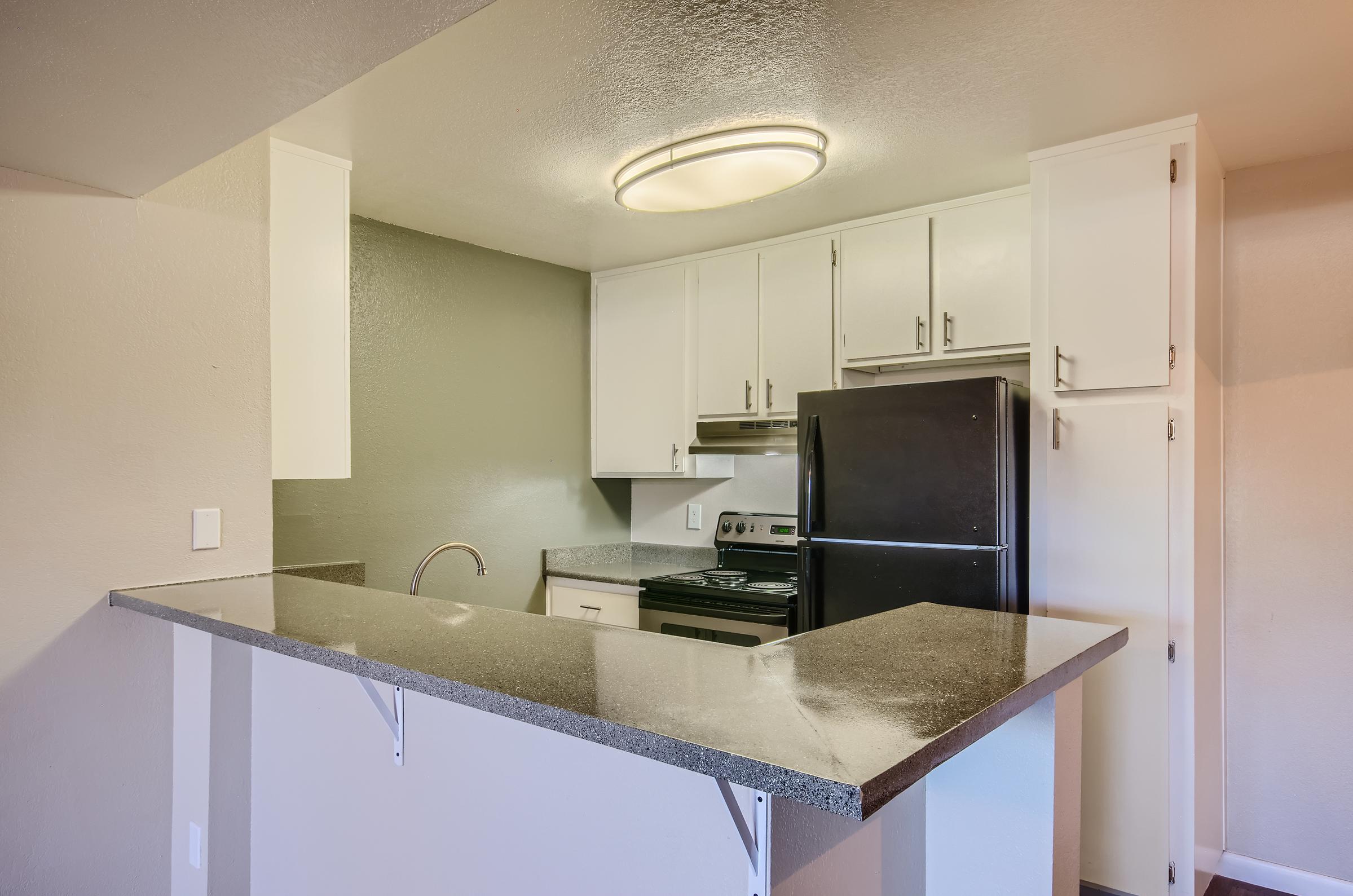 An apartment kitchen with white cabinets and black appliances at Rise on McClintock.
