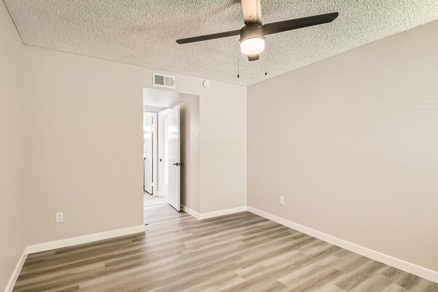 A bedroom with wood-style flooring and a ceiling fan near the kitchen at Rise on McClintock.