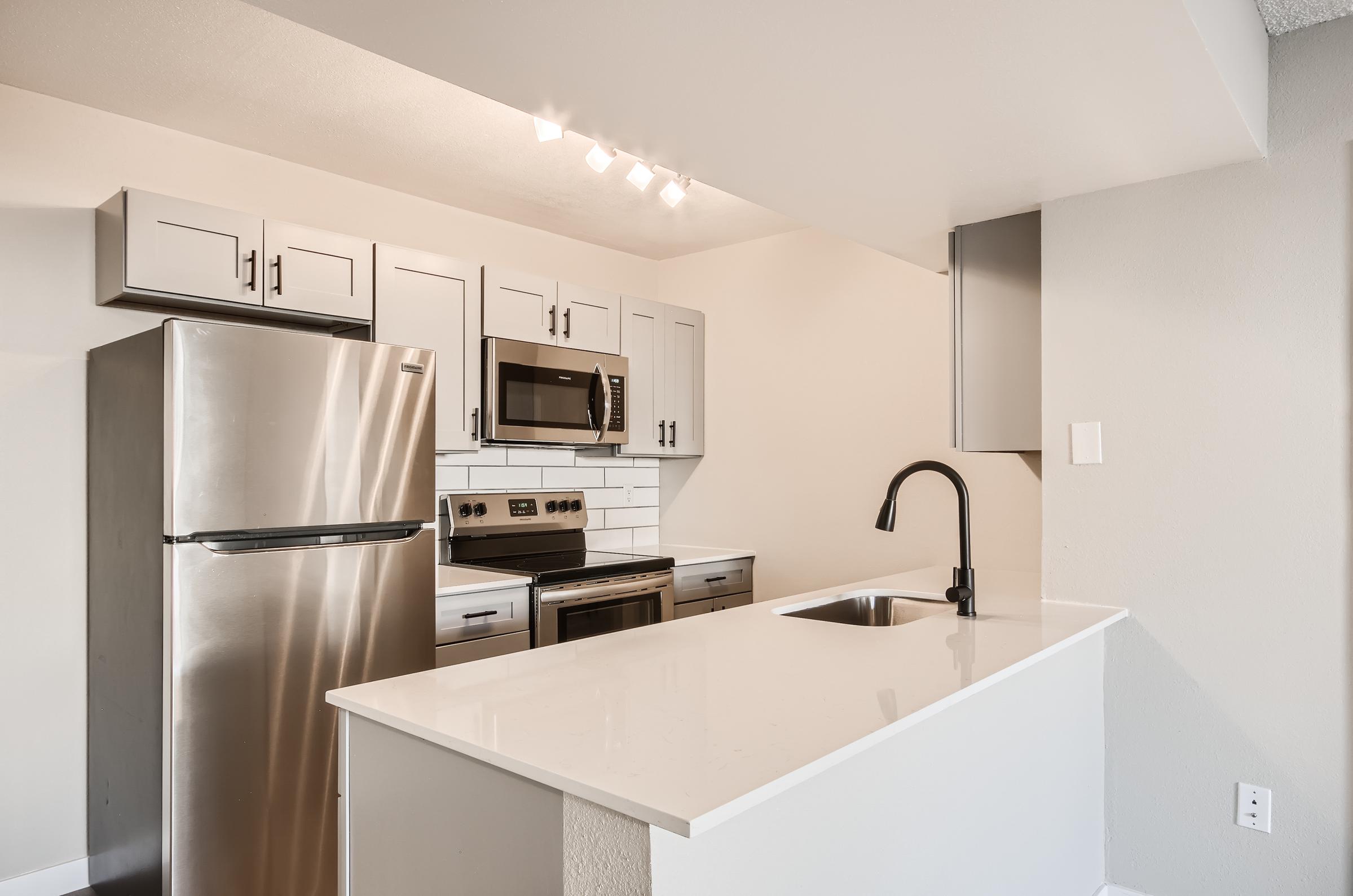A remodeled kitchen at Rise on McClintock with quartz countertops, stainless steel appliances, and white shaker cabinets.