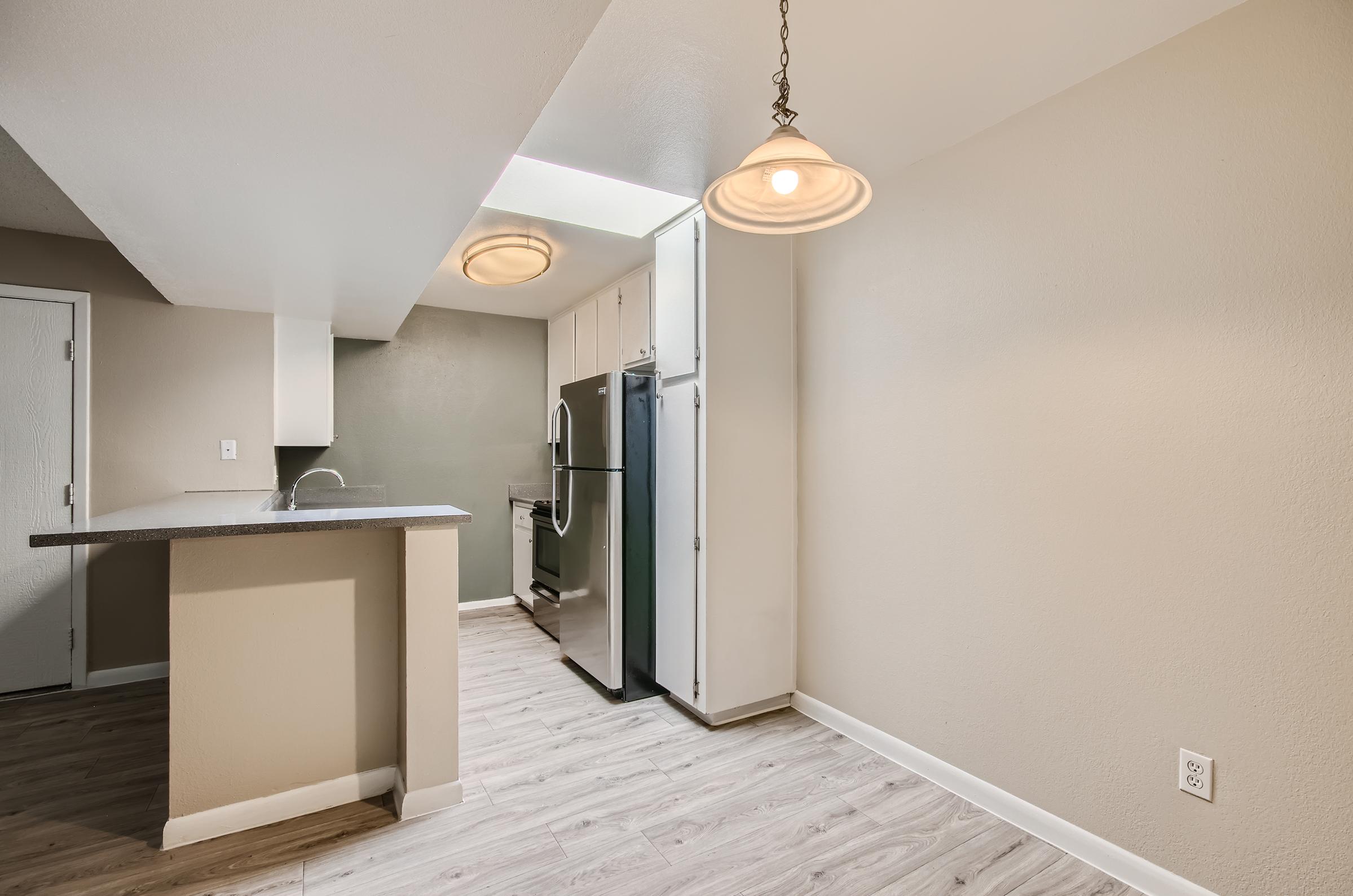 An apartment kitchen and dining area with hanging lighting and wood-style flooring at Rise on McClintock.