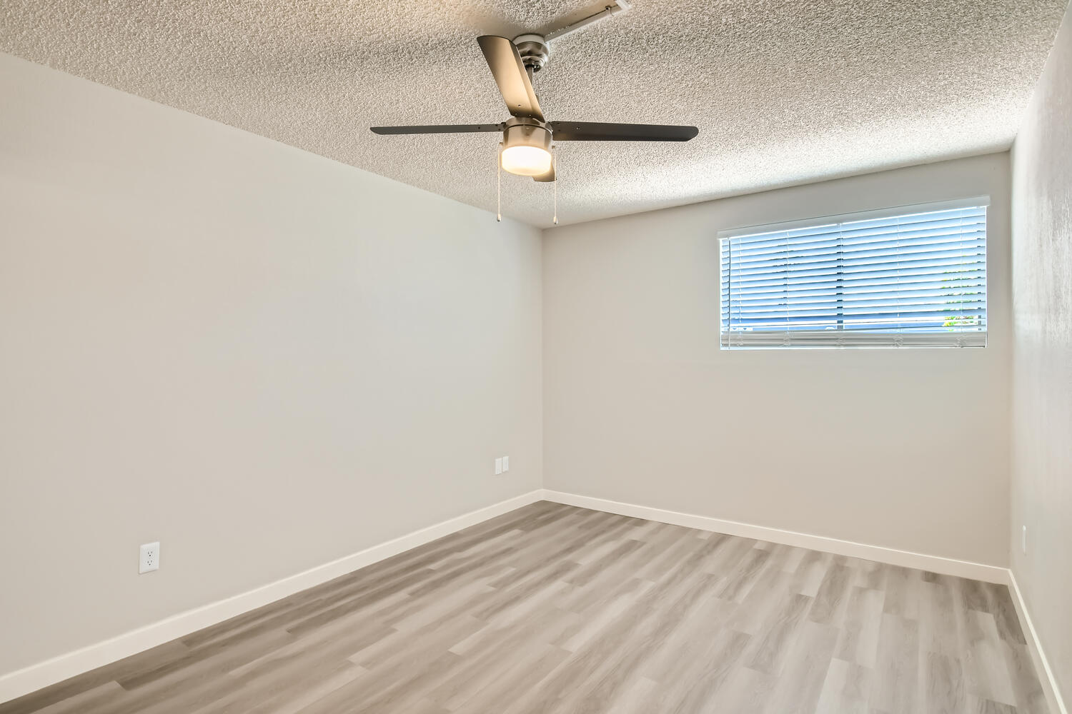 An apartment bedroom with wood-style flooring, a ceiling fan, and a window at Rise on McClintock.