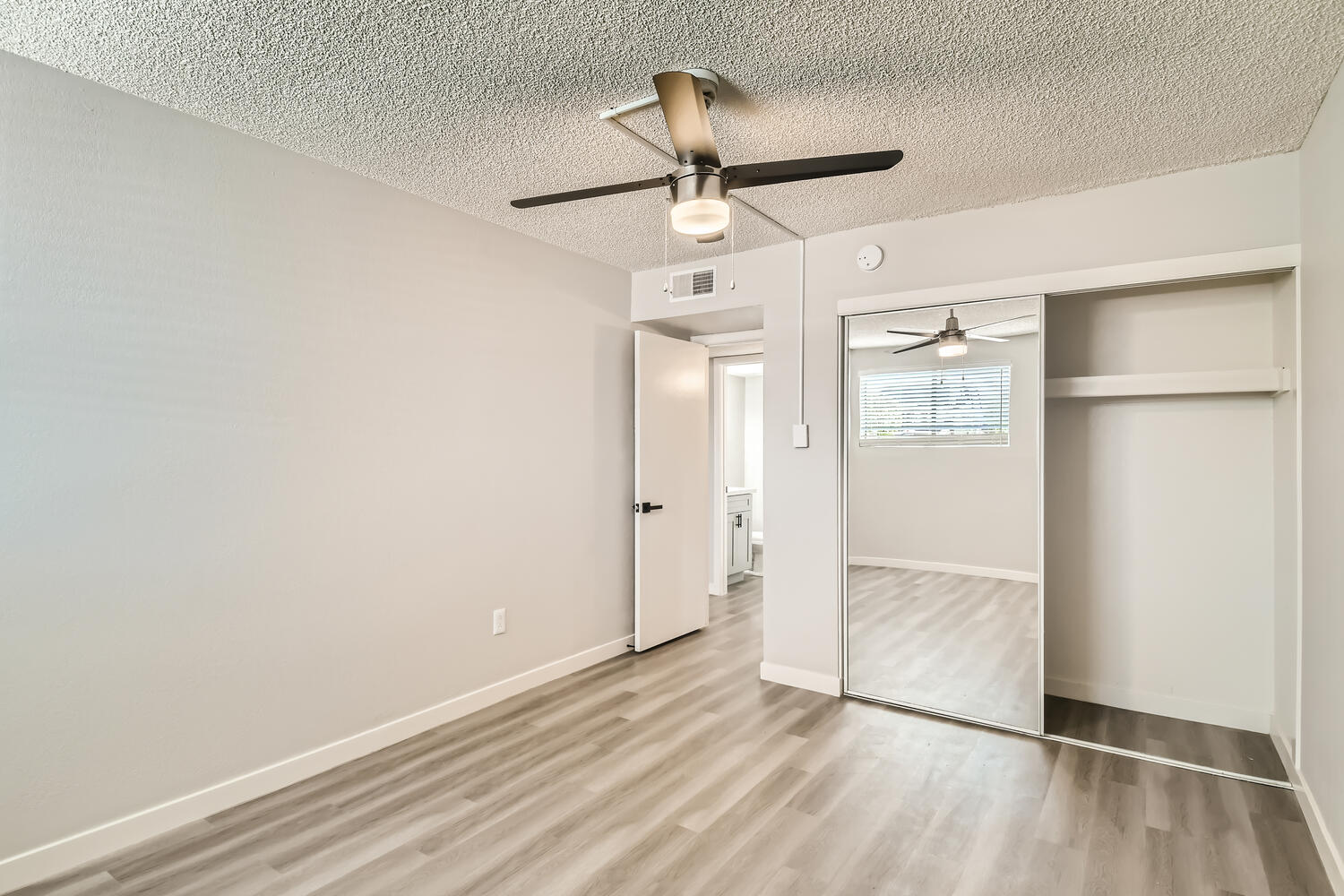 An apartment bedroom with wood-style flooring and a ceiling fan at Rise on McClintock.