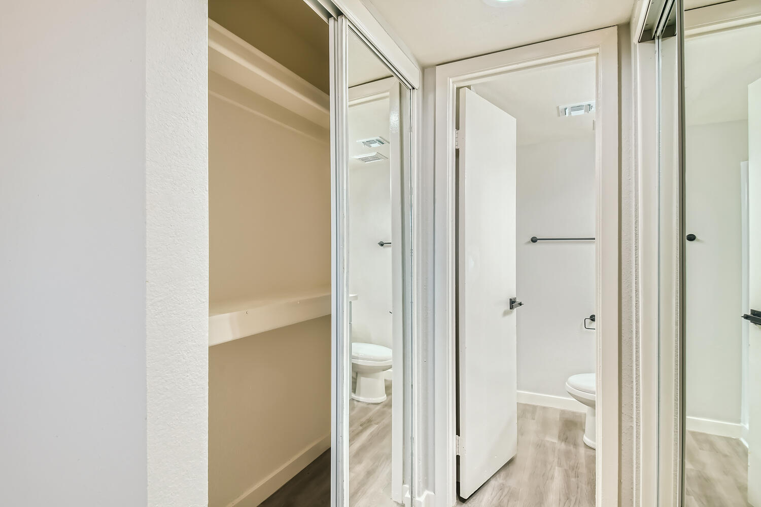 An open bedroom closet leading to the en-suite bathroom in an apartment at Rise on McClintock.
