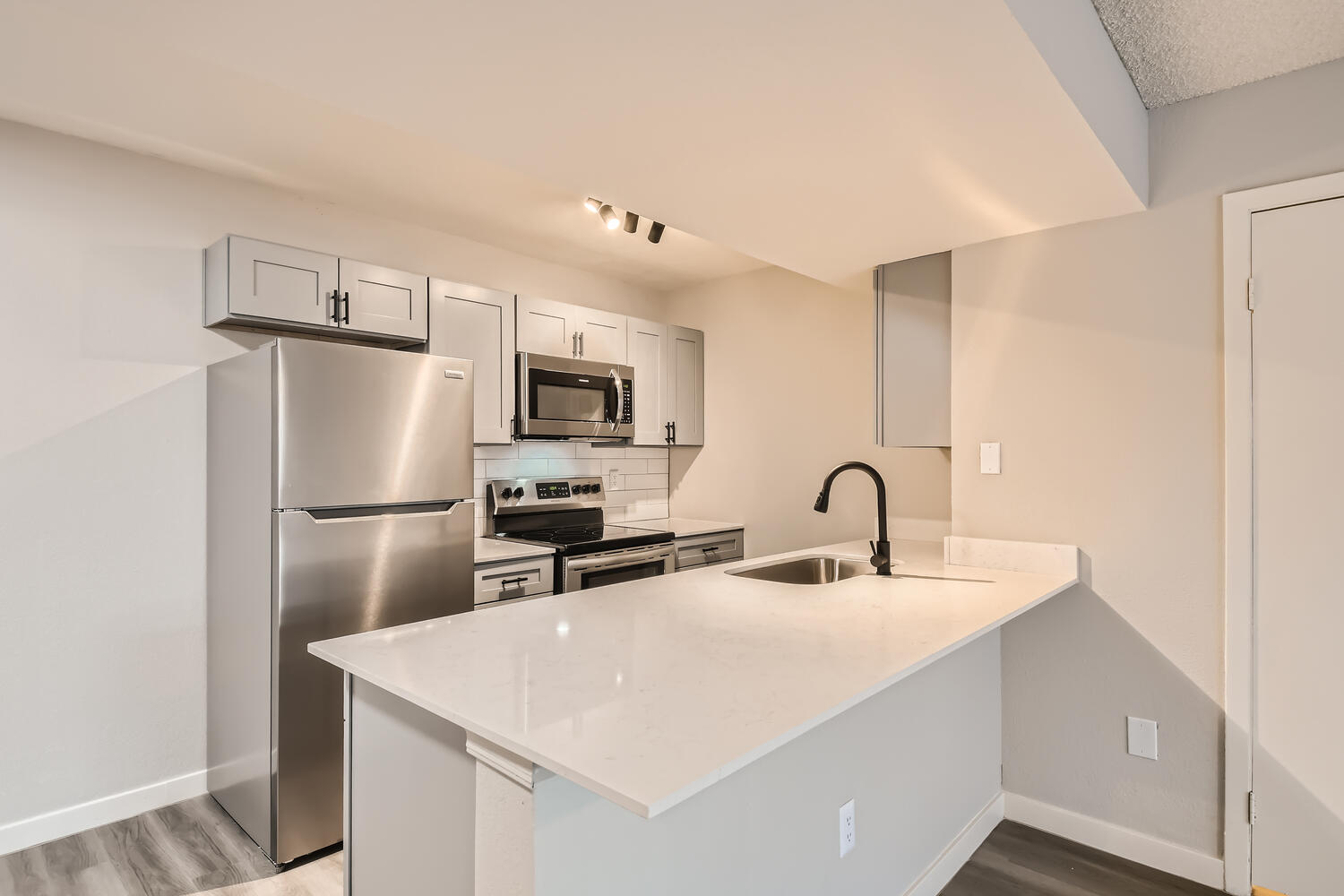 The kitchen in an apartment at Rise on McClintock with quartz countertops, white shaker cabinets, and stainless steel appliance.
