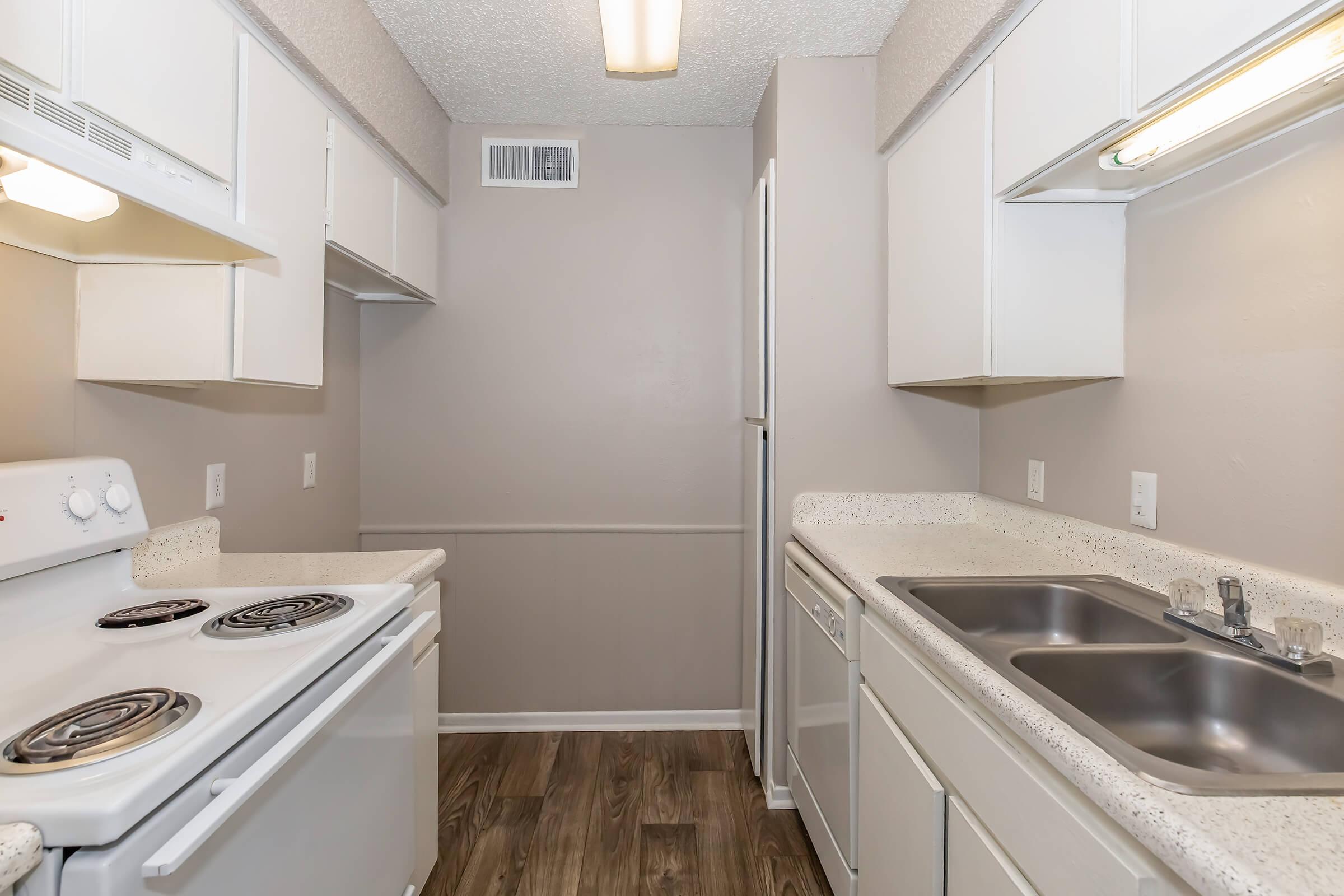 A clean, modern kitchen featuring white cabinets, a stove with two burners, a double sink, and a refrigerator. The walls are painted in neutral tones, and the floor has a wood-like design. Ample counter space is available for meal preparation, creating a functional kitchen environment.