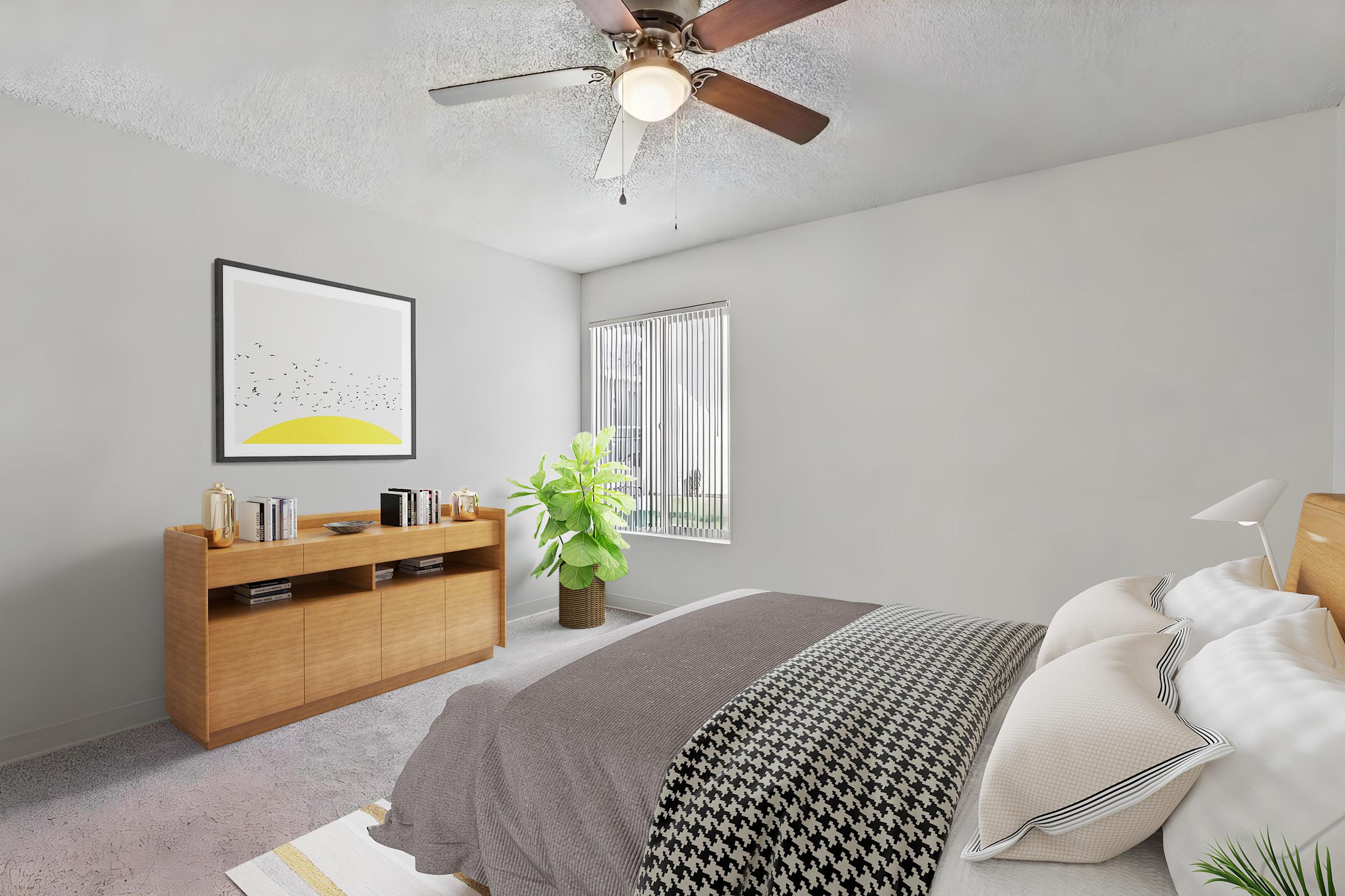 A modern bedroom featuring a bed with gray and white bedding, a wooden nightstand, and a large window with vertical blinds. A decorative plant adds greenery, and a piece of abstract art hangs on the wall above a wooden dresser with books and decorative items. The ceiling has a ceiling fan.