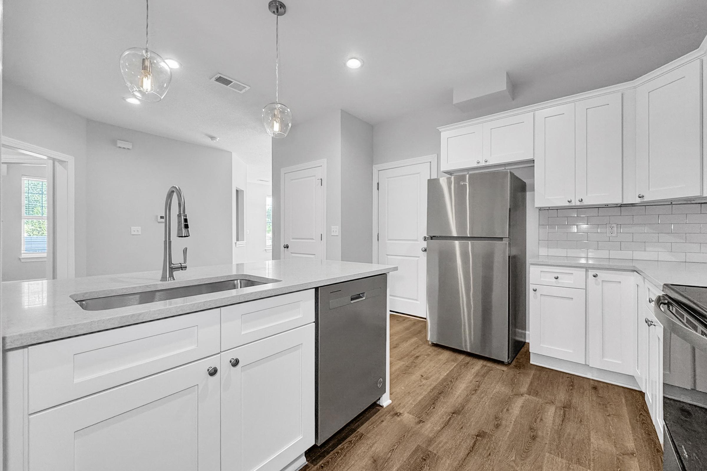 Modern kitchen featuring white cabinetry, stainless steel appliances including a refrigerator and dishwasher, a sleek sink with a pull-down faucet, and light wood flooring. The space is bright with natural light from nearby windows, creating a clean and inviting atmosphere.