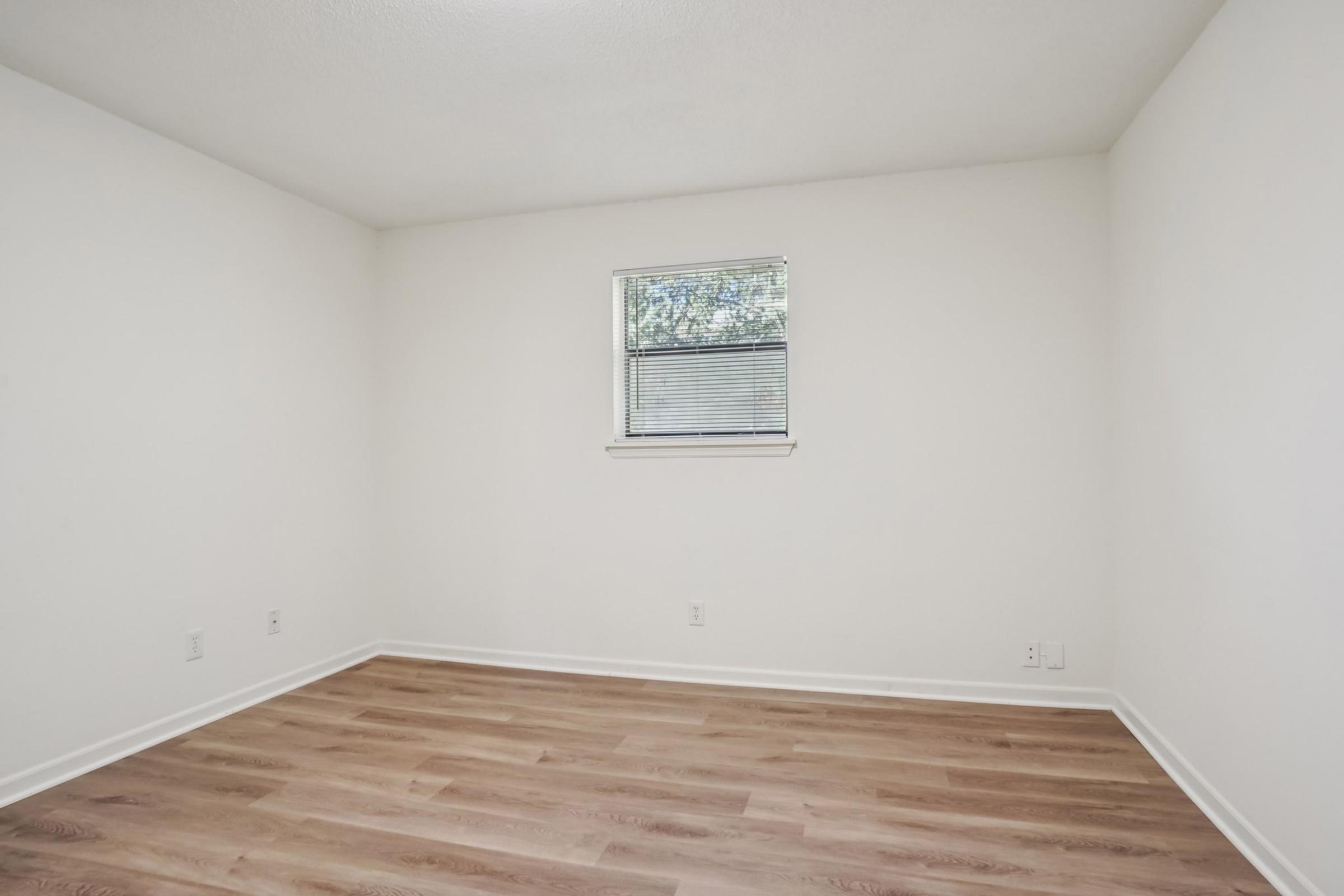 Empty room with light-colored walls and a small window. The floor is covered in light brown laminate. There are no furnishings or decorations, creating a spacious and minimalistic appearance.