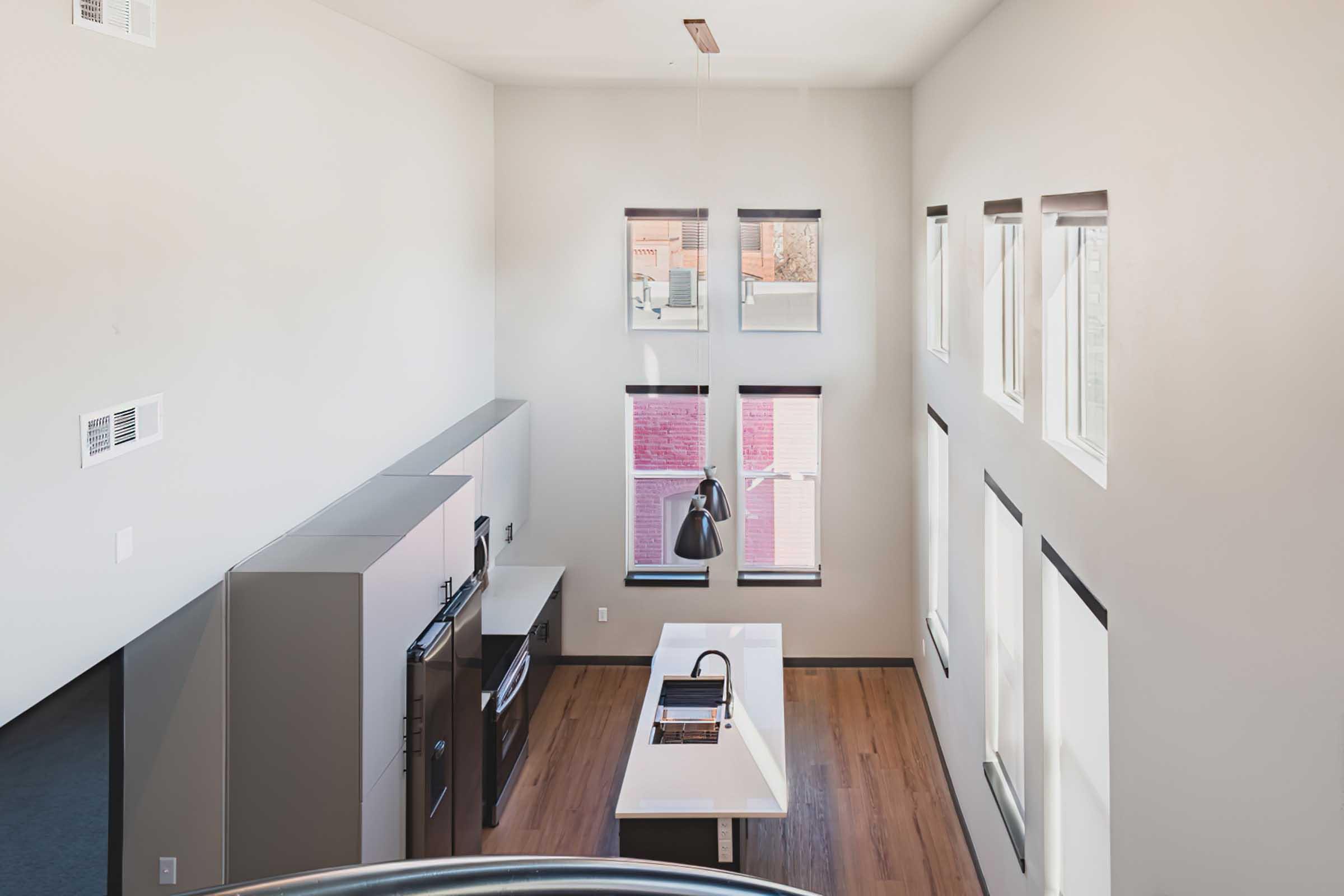 A modern kitchen with a minimalist design, featuring a central island, sleek appliances, and large windows that allow natural light to fill the space. The walls are painted in a light color, and the wooden floor adds warmth to the overall aesthetic.