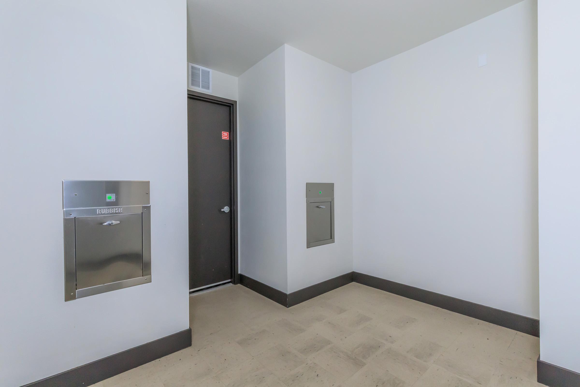 A clean, modern hallway featuring two mailboxes mounted on the wall. A plain door is visible at the end of the hallway, and the walls are painted in a light color. The floor is tiled with a light-colored material, creating a bright and open atmosphere.