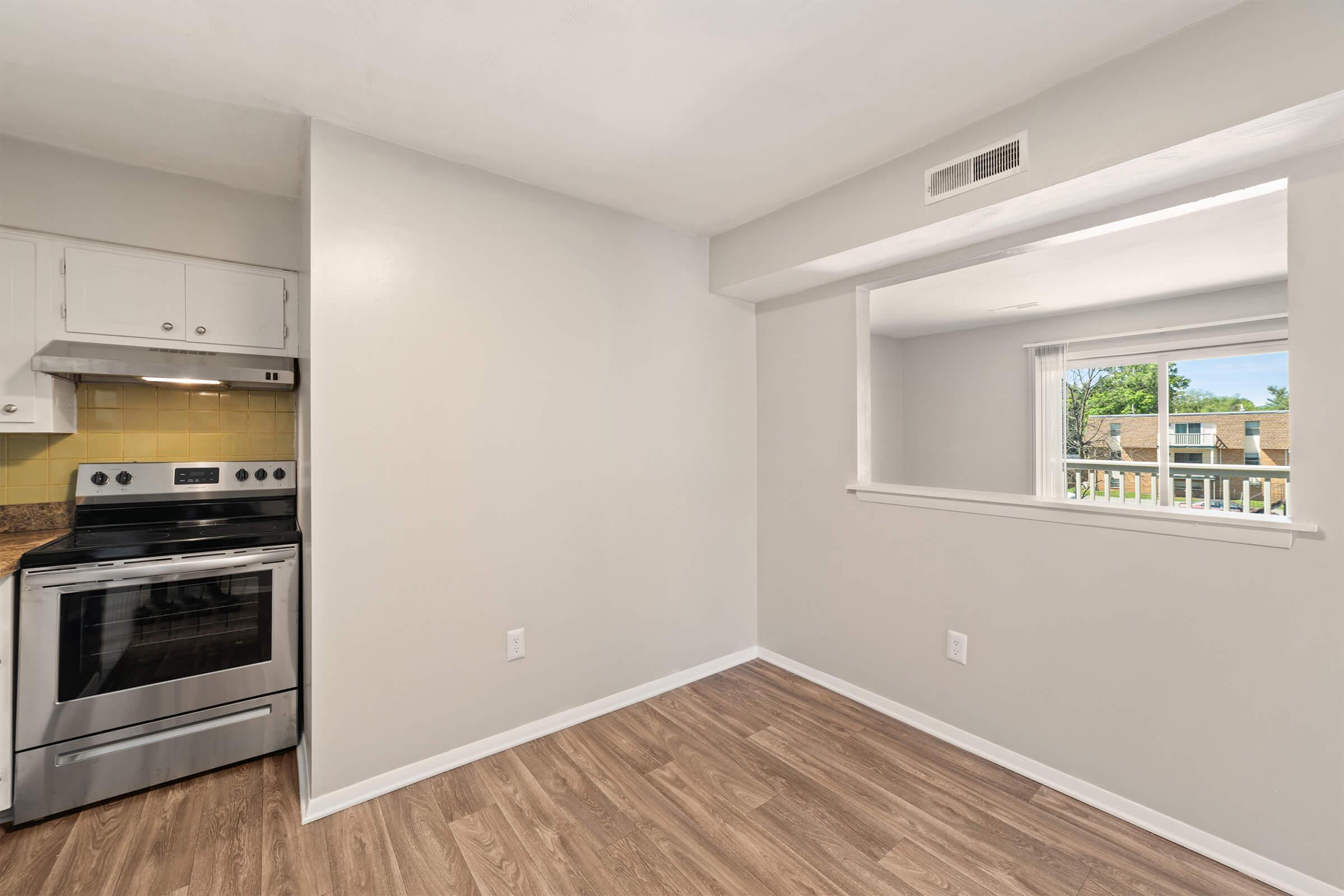 Modern kitchen featuring stainless steel appliances, including an oven and stovetop, against a light gray wall. The room has a window providing natural light and a view to the outside. Light wood flooring complements the space, which has a clean and contemporary design.