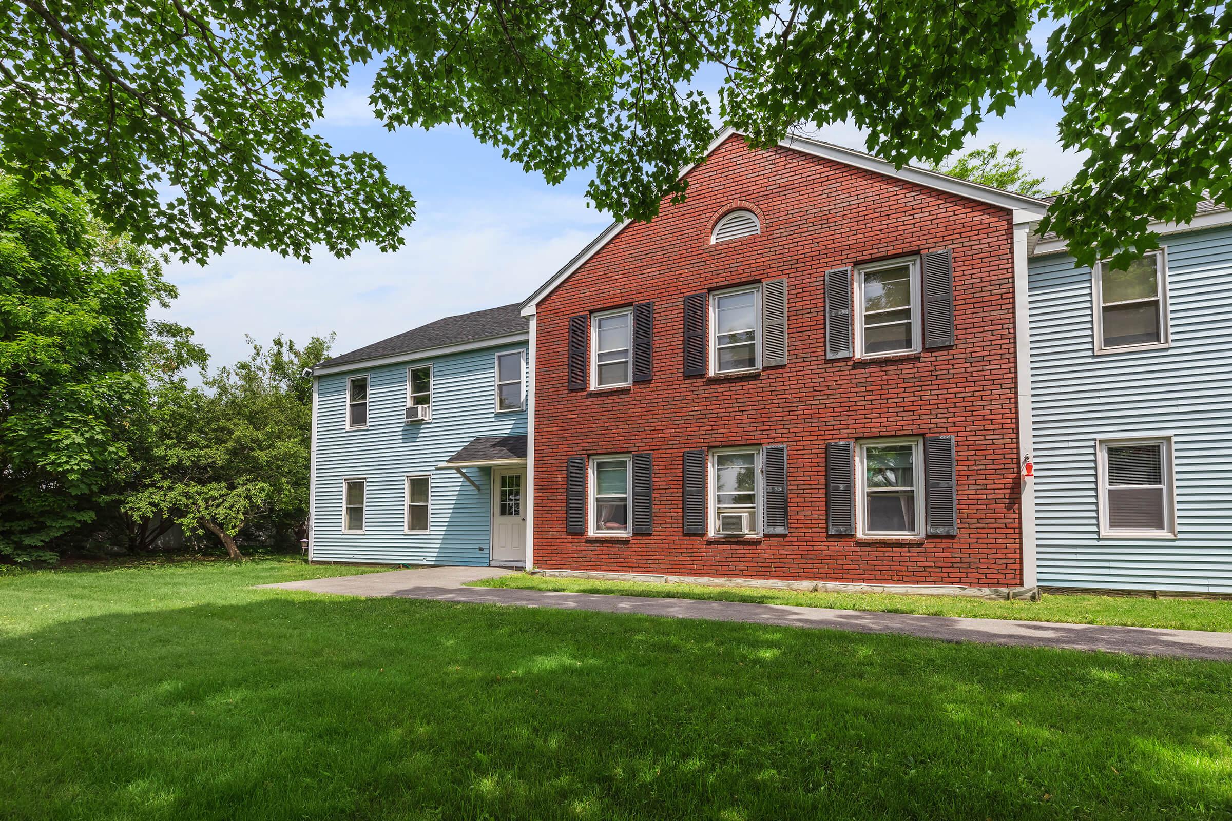 a large brick building with grass in front of a house with Munroe Tavern in the background