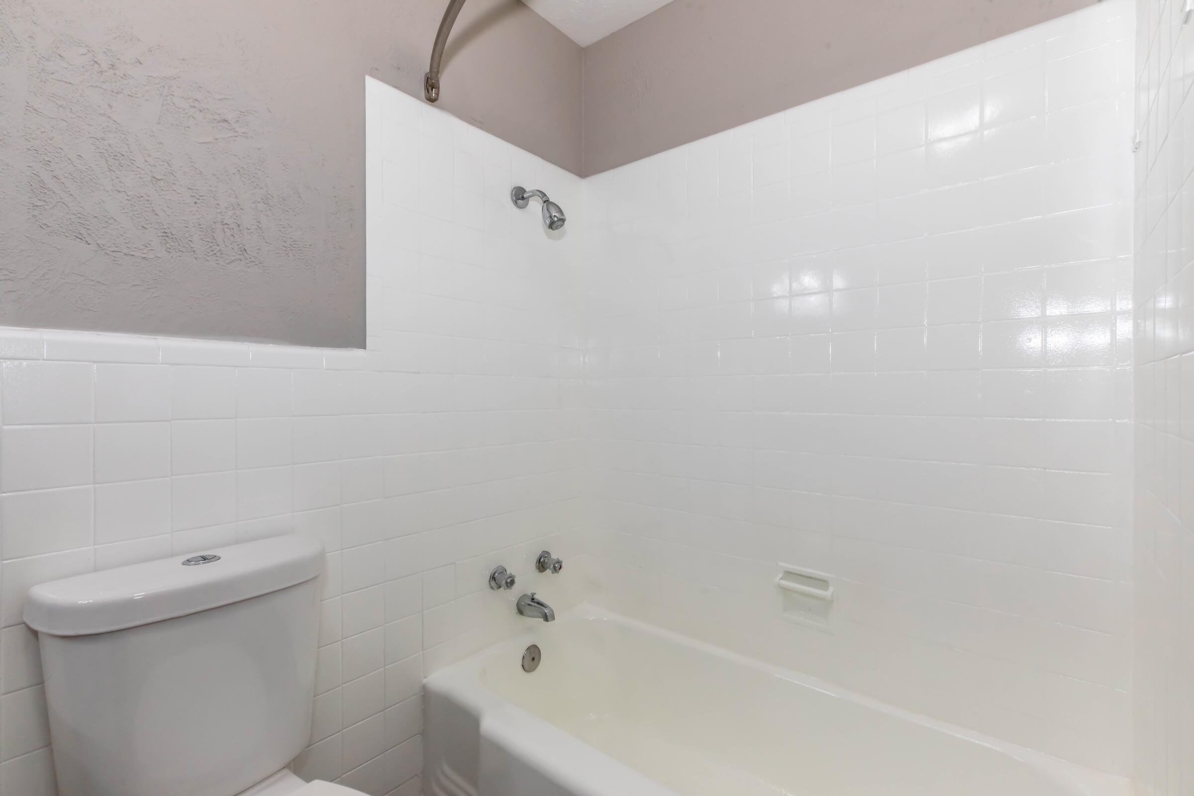 A clean, modern bathroom featuring a white bathtub, a toilet, and a tile shower area with a mounted showerhead. The walls are painted in a soft color, creating a bright and airy atmosphere. The space is uncluttered and designed for functionality.