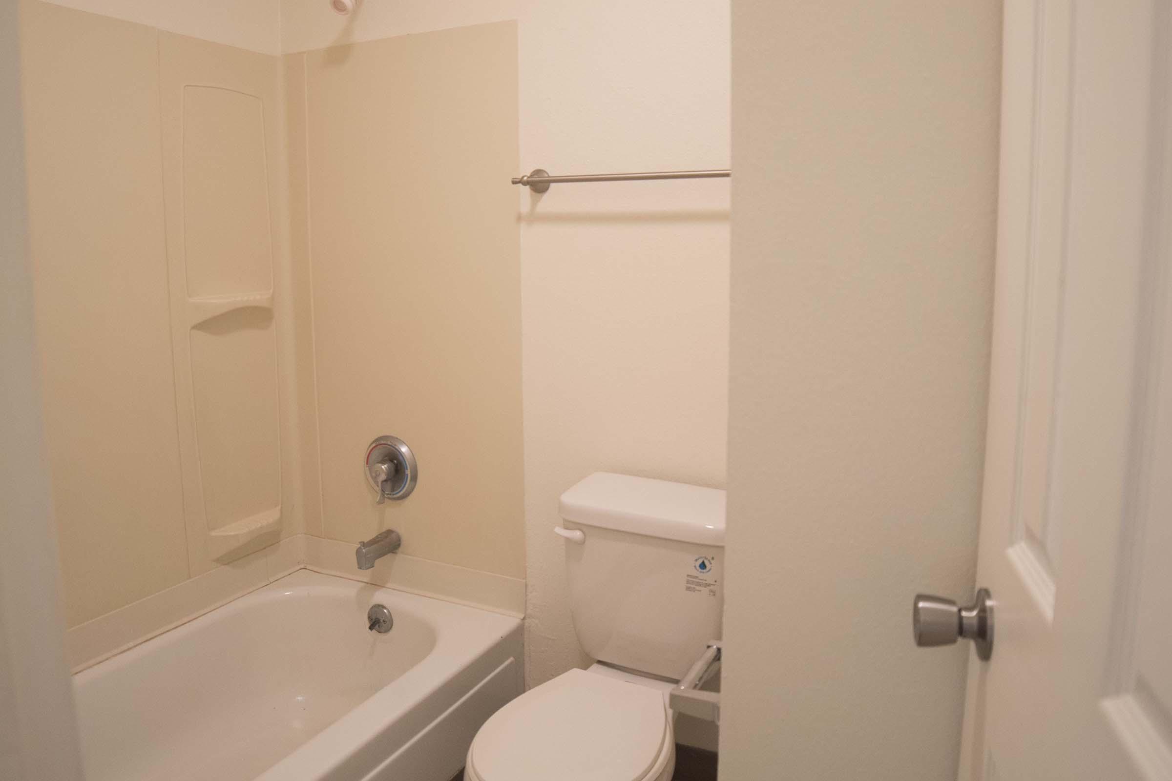 A small bathroom featuring a bathtub with a showerhead, a toilet, and a towel bar mounted on the wall. The walls are painted a light color, and the space appears clean and minimally decorated.