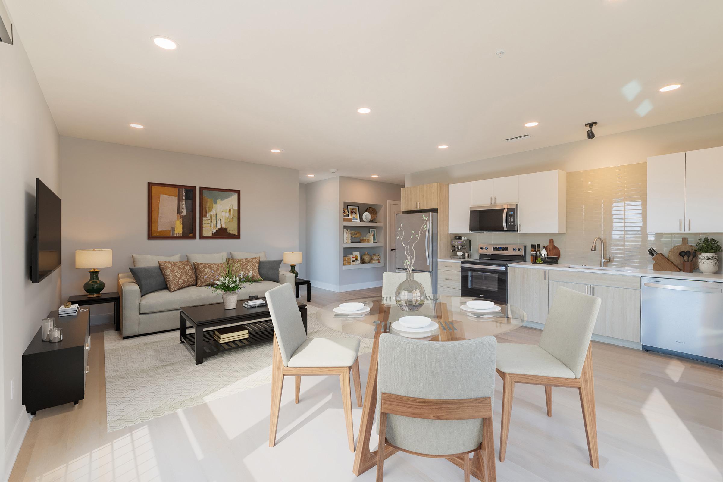 A modern living space featuring a cozy seating area with a light gray sofa, a glass dining table set for four, and a well-equipped kitchen. The decor is contemporary, with neutral colors and tasteful artwork on the walls, creating a welcoming atmosphere.