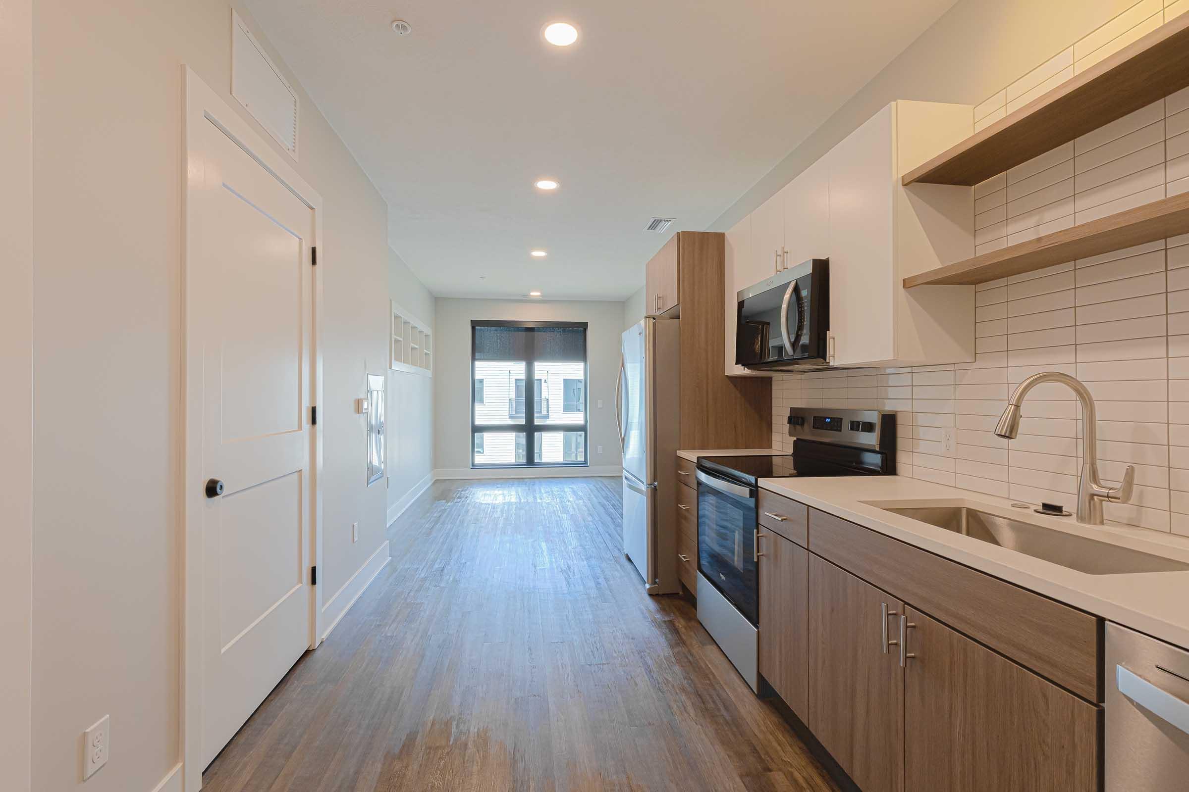 Modern kitchen featuring a combination of light and dark cabinetry, stainless steel appliances, a sink with a sleek faucet, and a tiled backsplash. The space includes a spacious open layout leading to a large window for natural light, and hardwood-style flooring.
