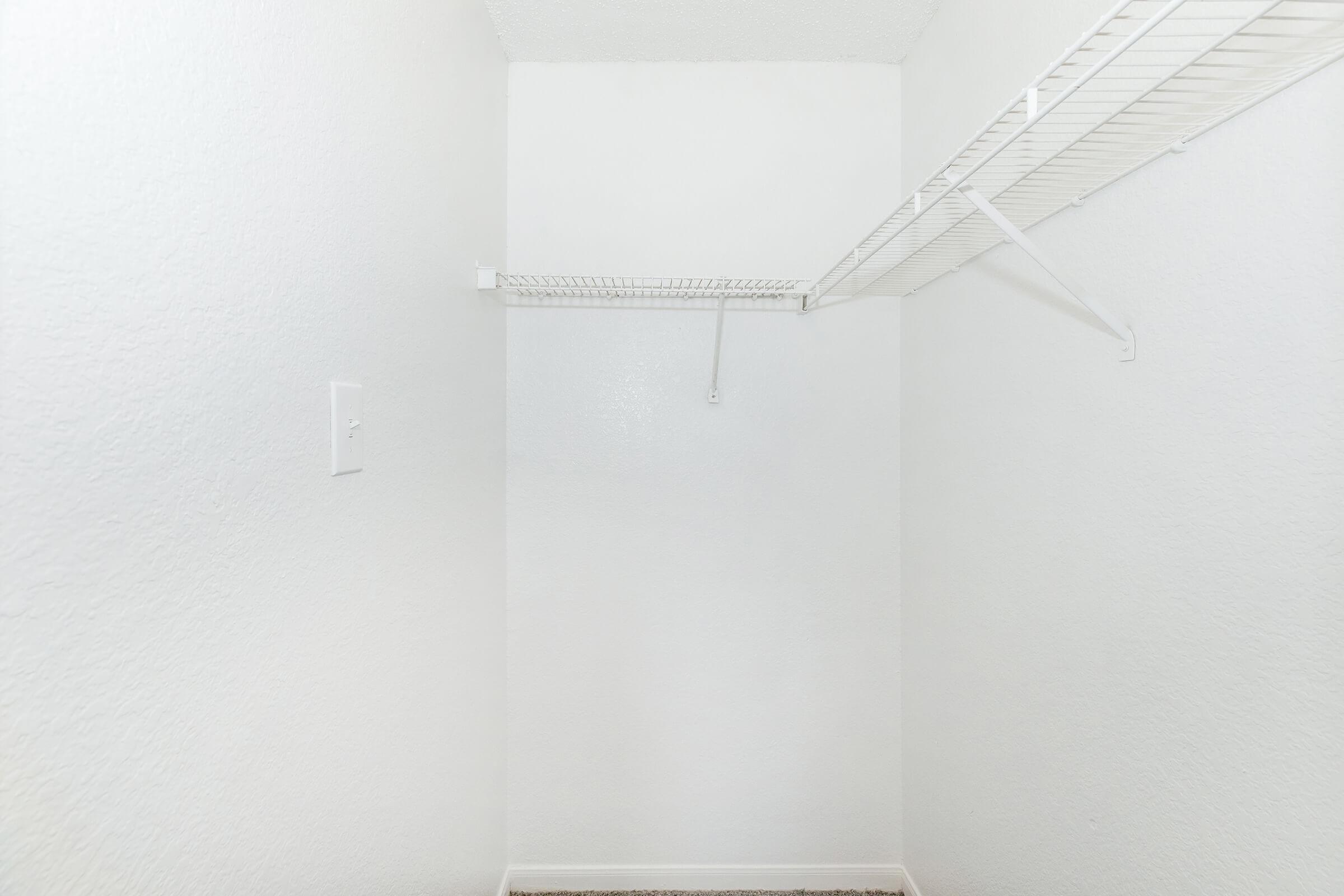 A clean, empty closet featuring white walls and a wire shelving unit. The space is minimalistic, with no items visible, creating an airy and uncluttered appearance.