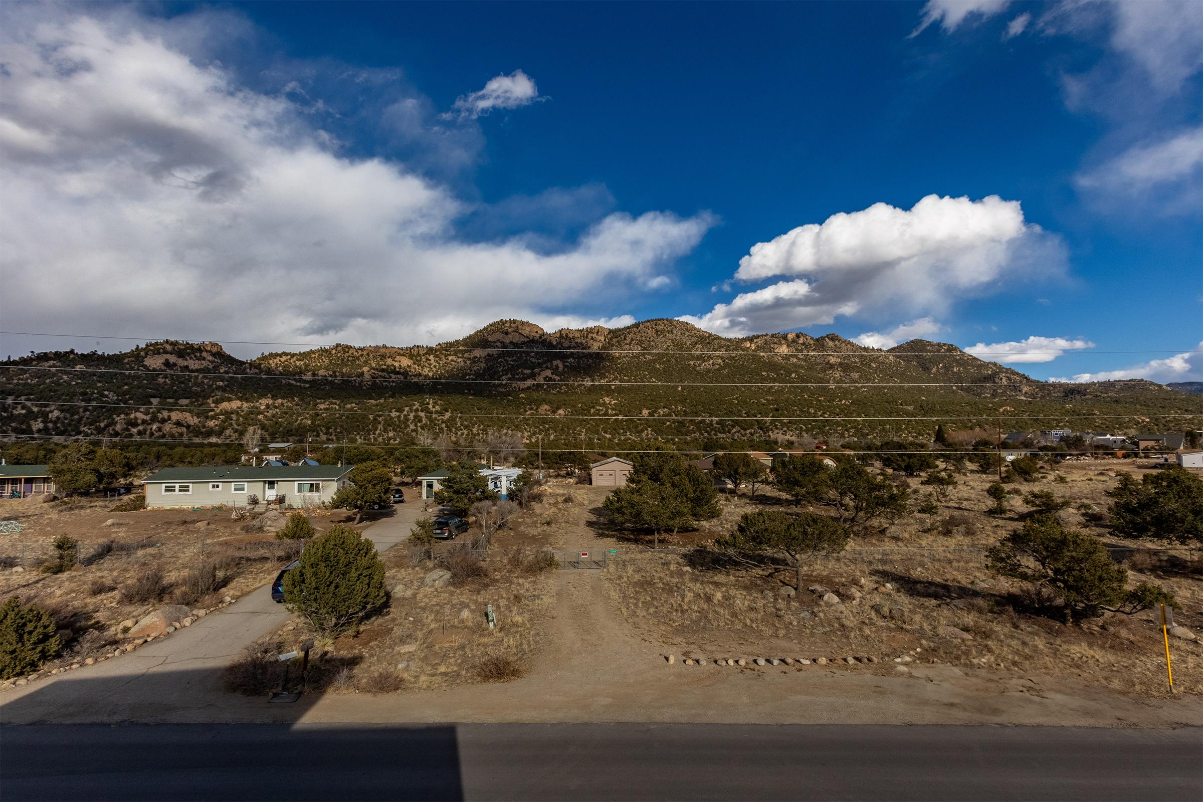 Scenic view of a rural landscape featuring low houses and sparse vegetation in the foreground, with rolling hills and mountains in the background. The sky is partly cloudy, showcasing a mix of blue and white clouds. The scene conveys a tranquil atmosphere typical of a mountainous region.