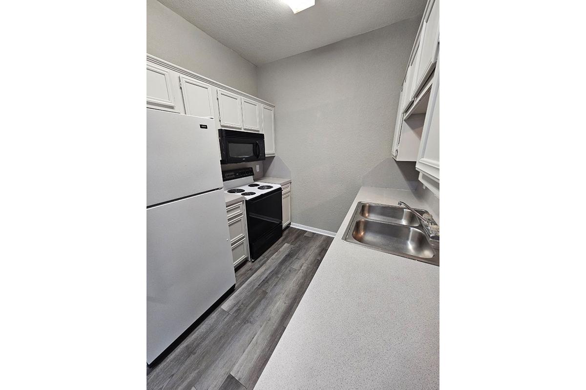 Modern kitchen featuring white cabinetry, a refrigerator, an electric oven, and a microwave. The countertops are light-colored, and the flooring is sleek and gray. The kitchen is well-lit, showcasing a clean and organized design with ample workspace.
