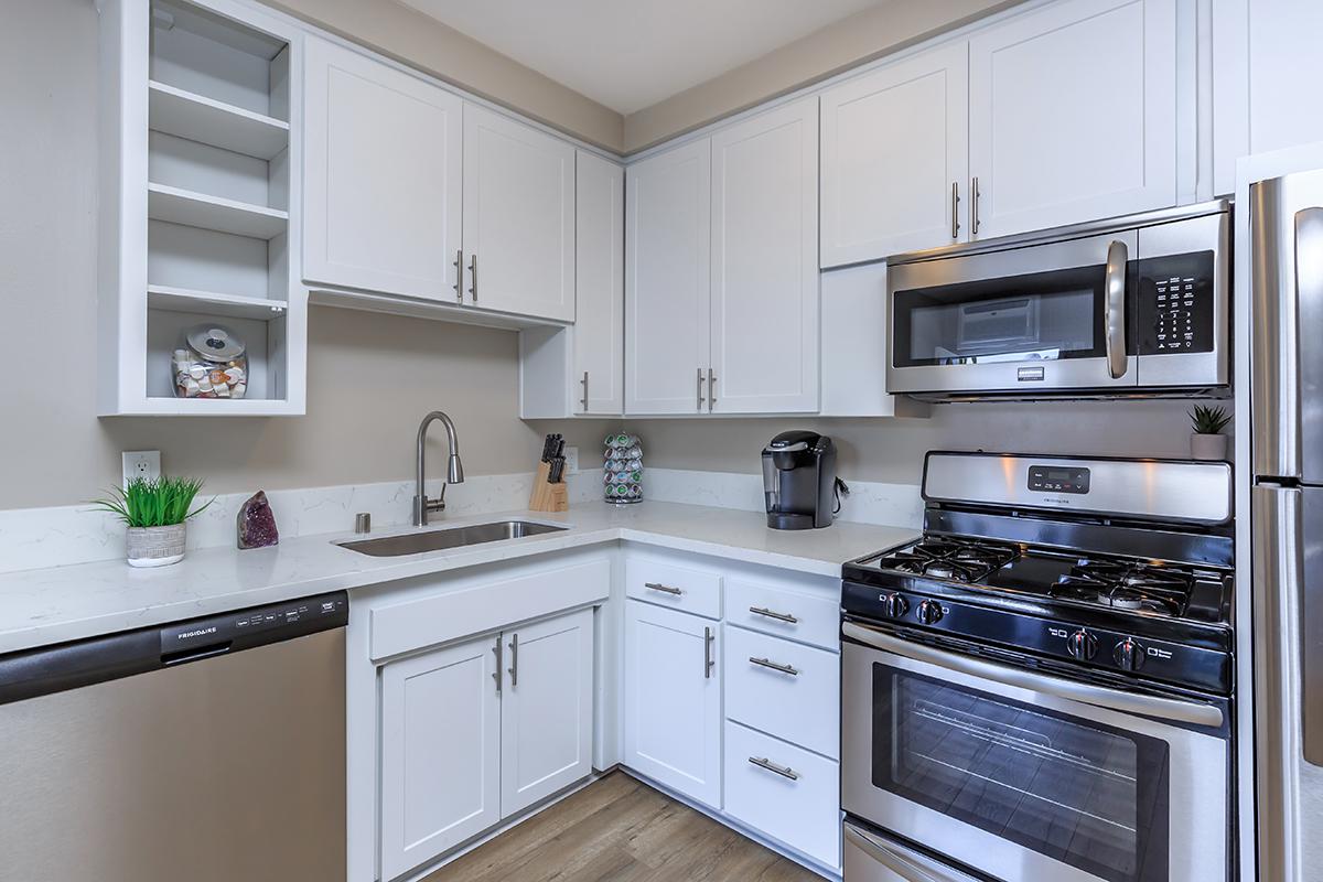Gas range with overhead microwave nestled among the white cabinets showing the goose necked faucet in our one bed one bath B floor plan
