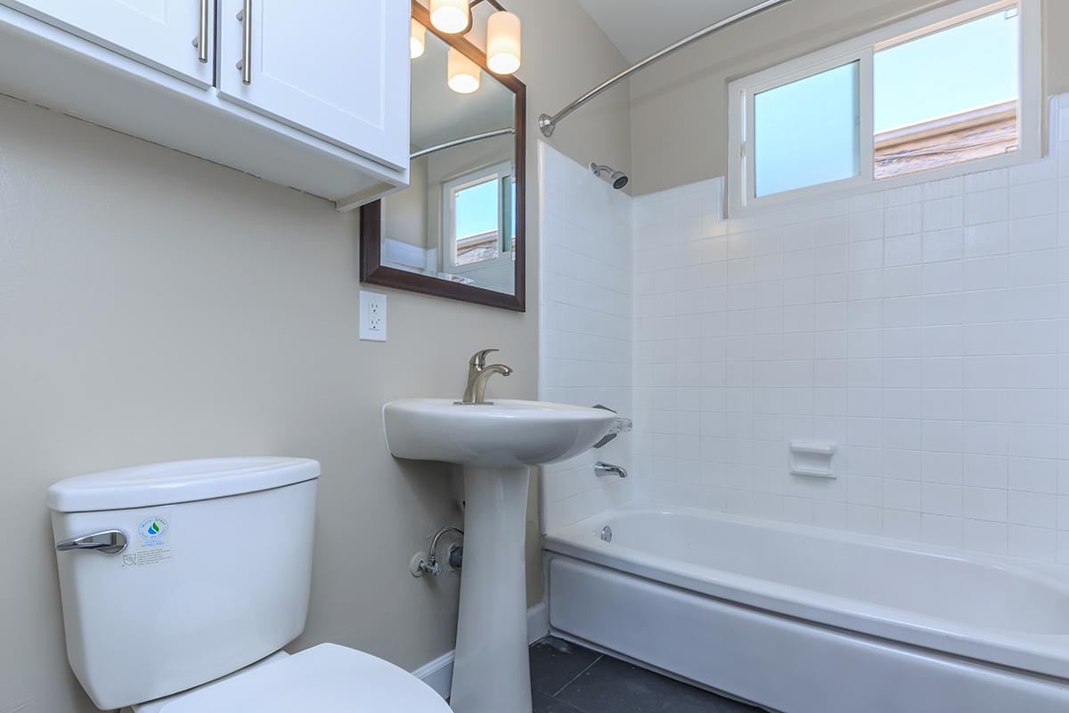 Great bathrooms at Flats on Elk have white surround in the tub-shower with a window and white storage cabinets above the commode.