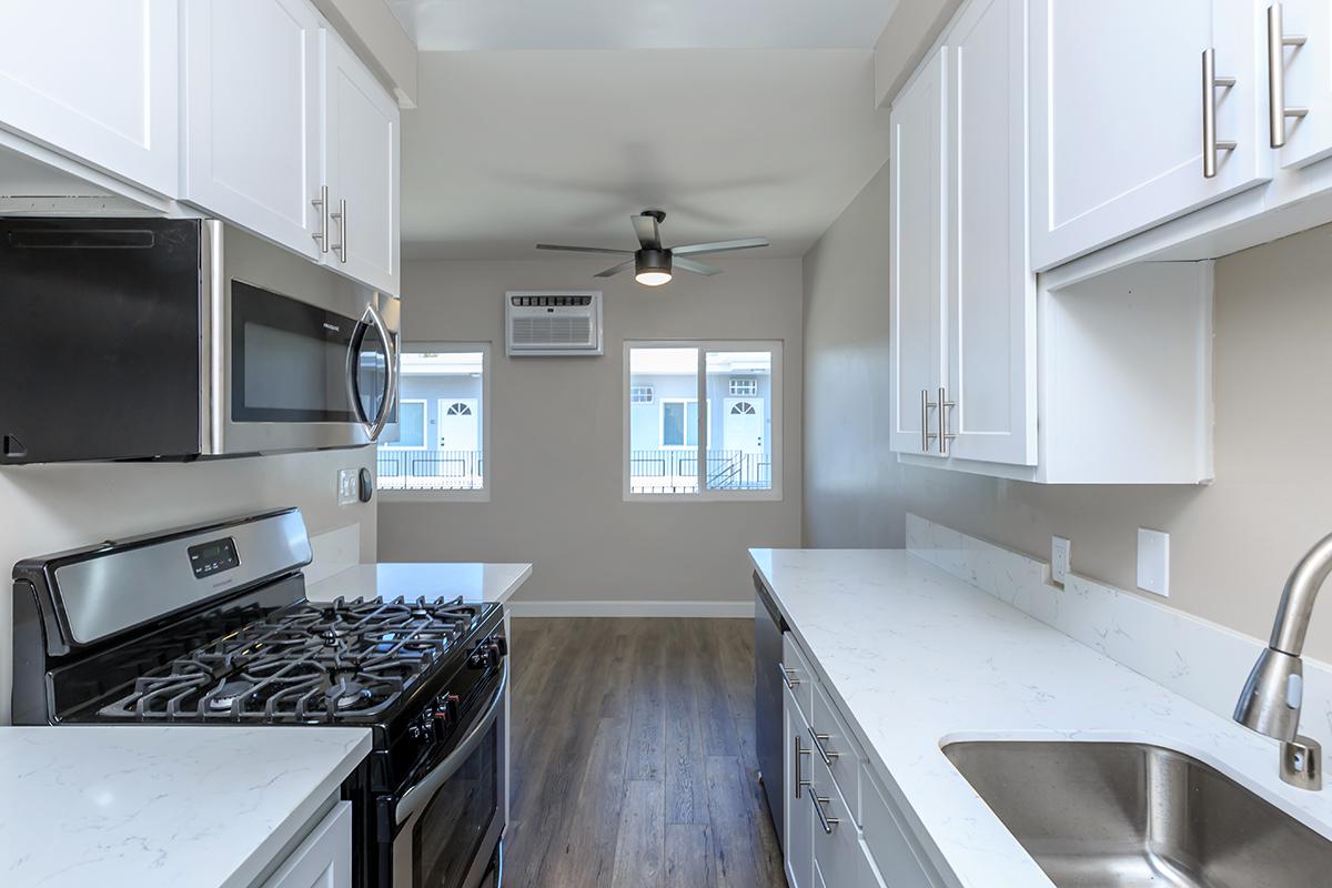 There is plenty of lighting in our one bed one bath D floor plan. This photo shows the white cabinets and countertops, goose neck faucet at the sink along with the gas range and over stove microwave.