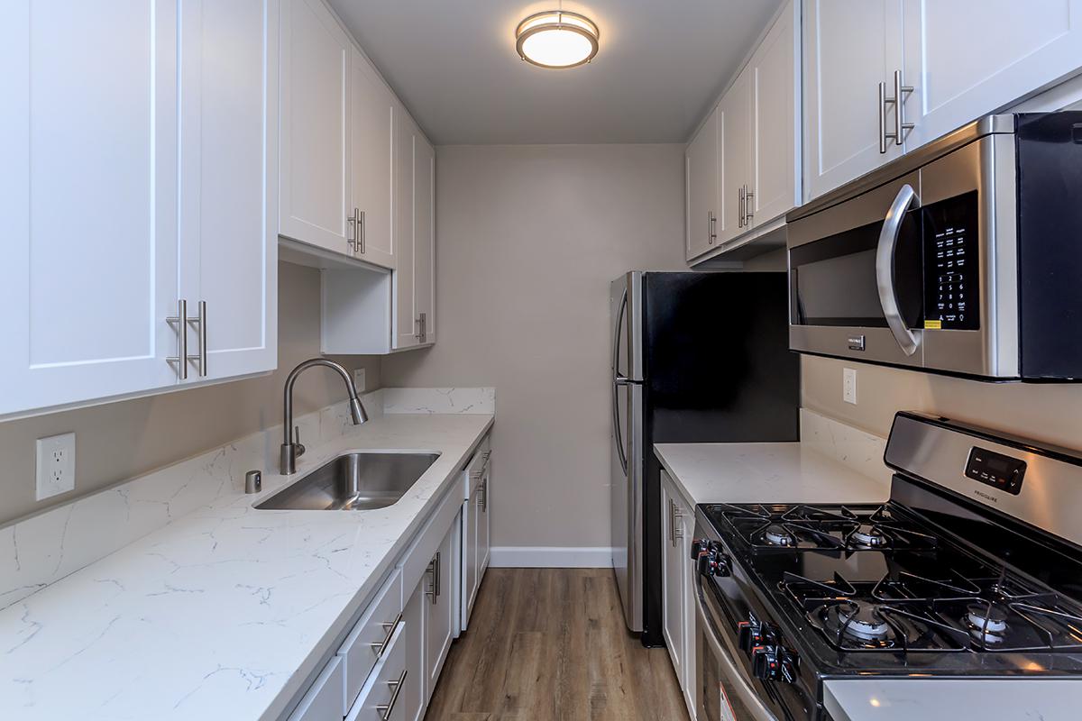 Stainless kitchen appliances at Flats on Elk make the white cabinets with white counters pop. There is also a goose neck faucet at the sink and the stove with overhead microwave to the front of the photo.