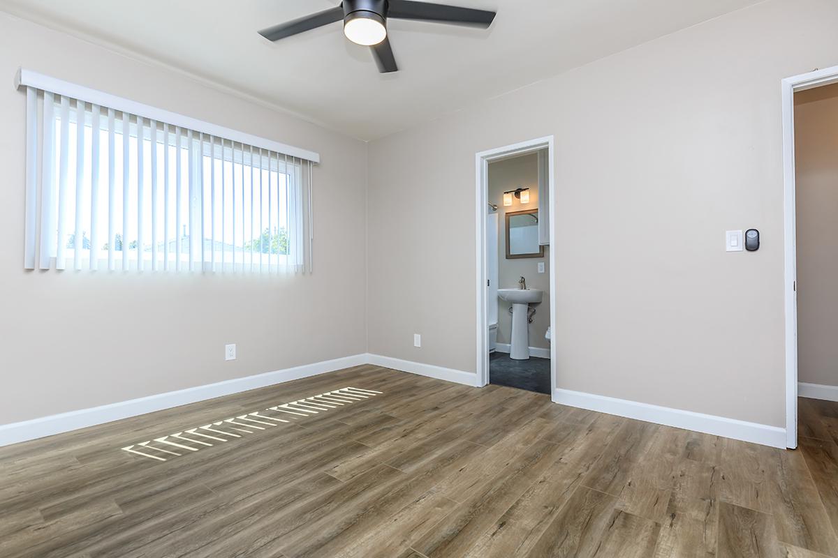 Wood-like floors, ceiling fans and vertical blinds in this photo of one of the bedrooms in our 2 bed 2 bath floor plan here at Flats on Elk.