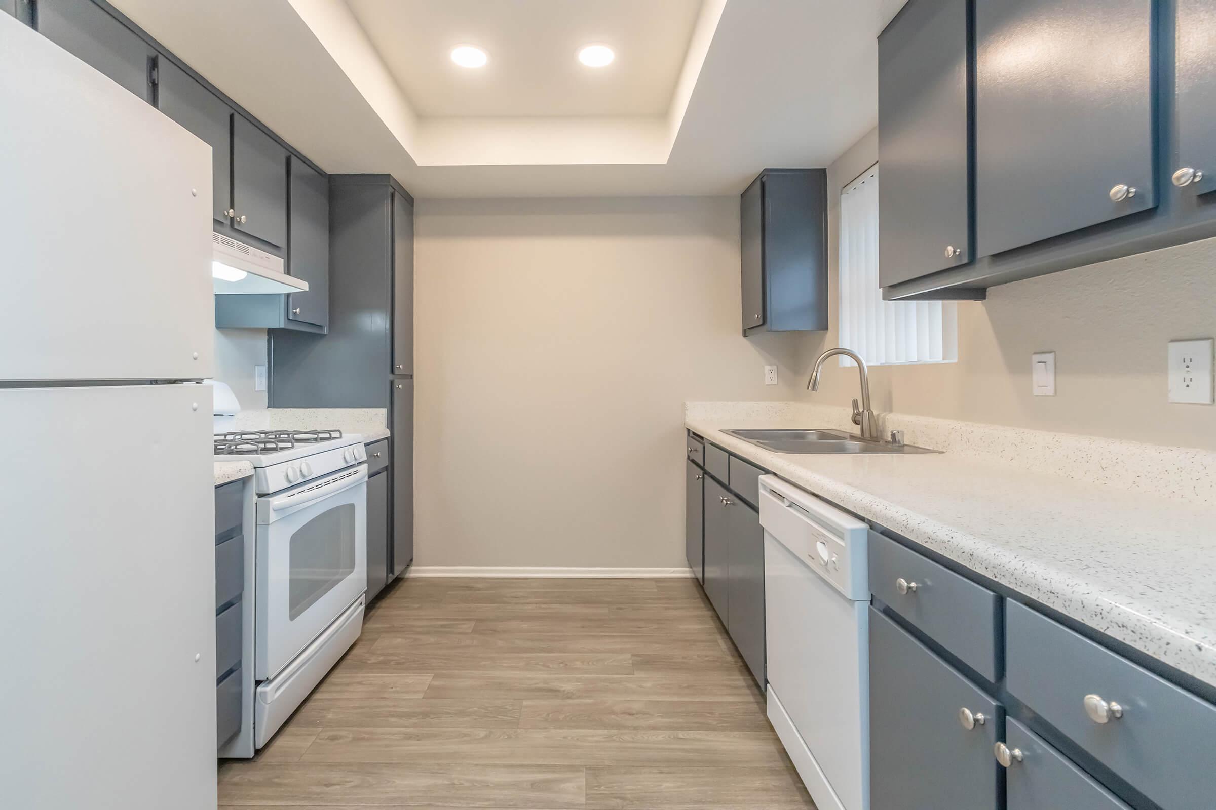 Modern kitchen featuring dark blue cabinets, white countertops, and stainless steel appliances. Includes a gas stove, dishwasher, and a double sink. The space is well-lit with recessed ceiling lights and has a neutral wall color. A window provides natural light, enhancing the overall ambiance.