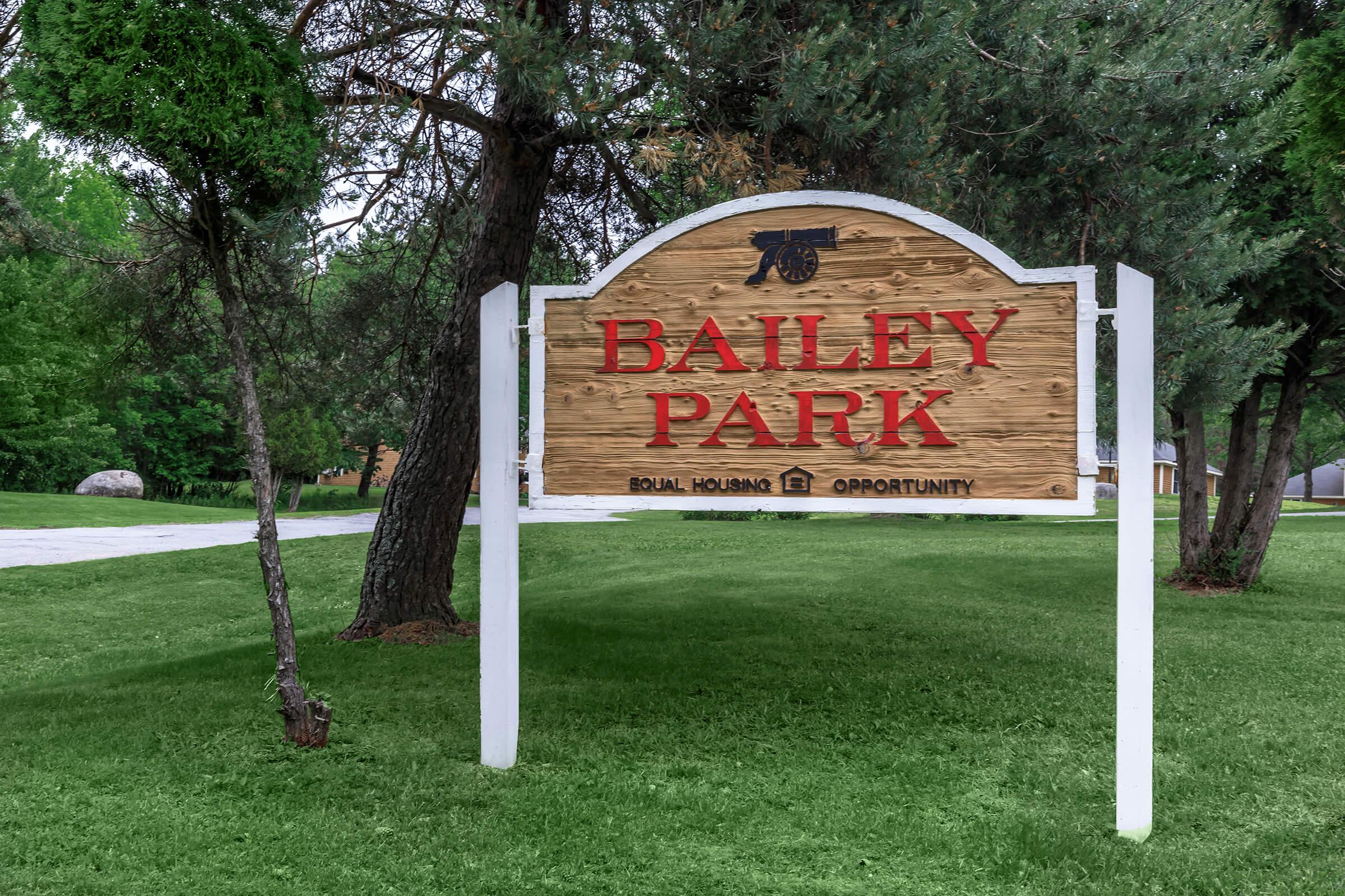 a sign over a grassy area with trees in the background