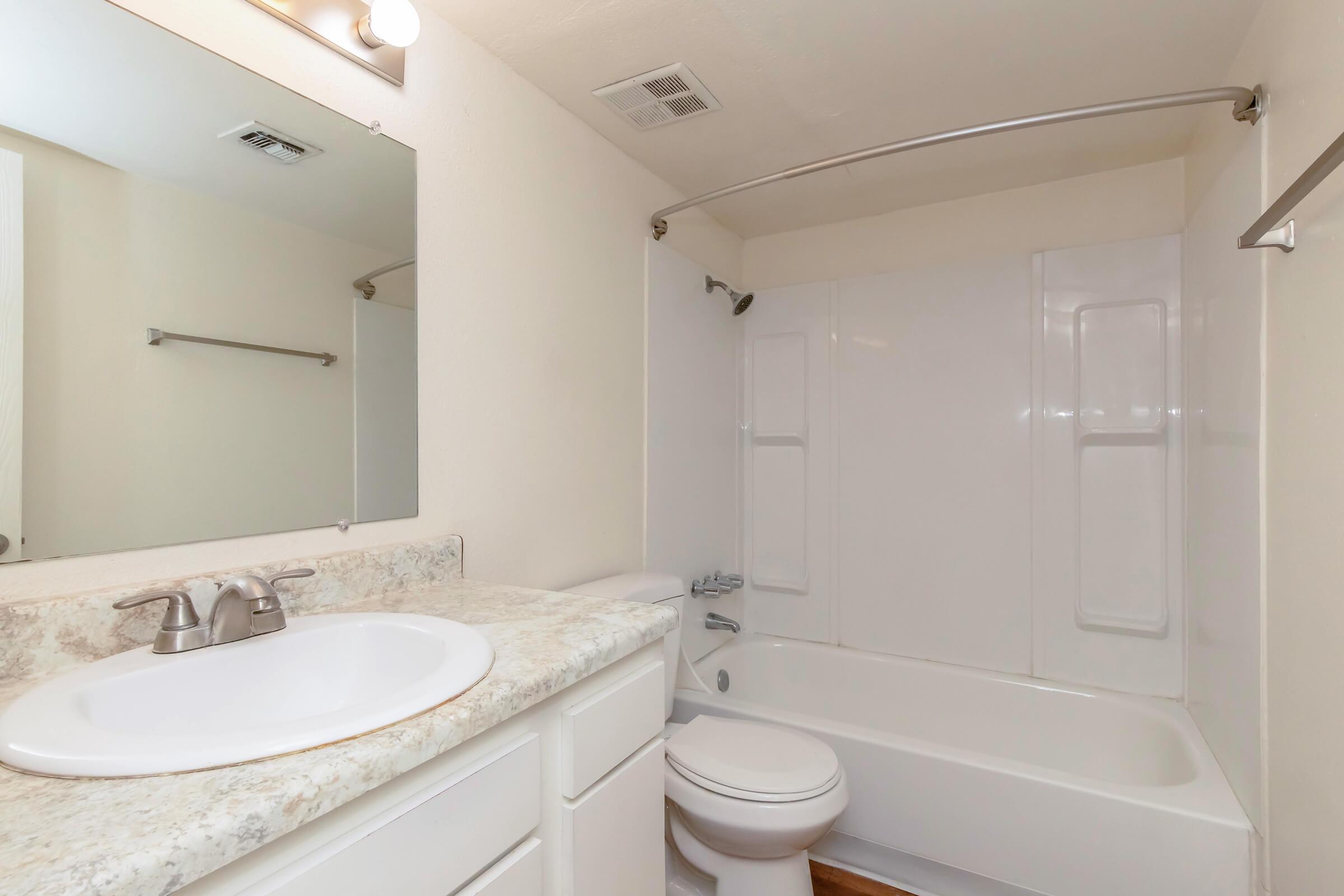 A clean and bright bathroom featuring a tub with shower, a white vanity with a circular sink, and a large mirror above the sink. The walls are light-colored, and the flooring is wood. The space is uncluttered and well-lit, giving a fresh, modern appearance.