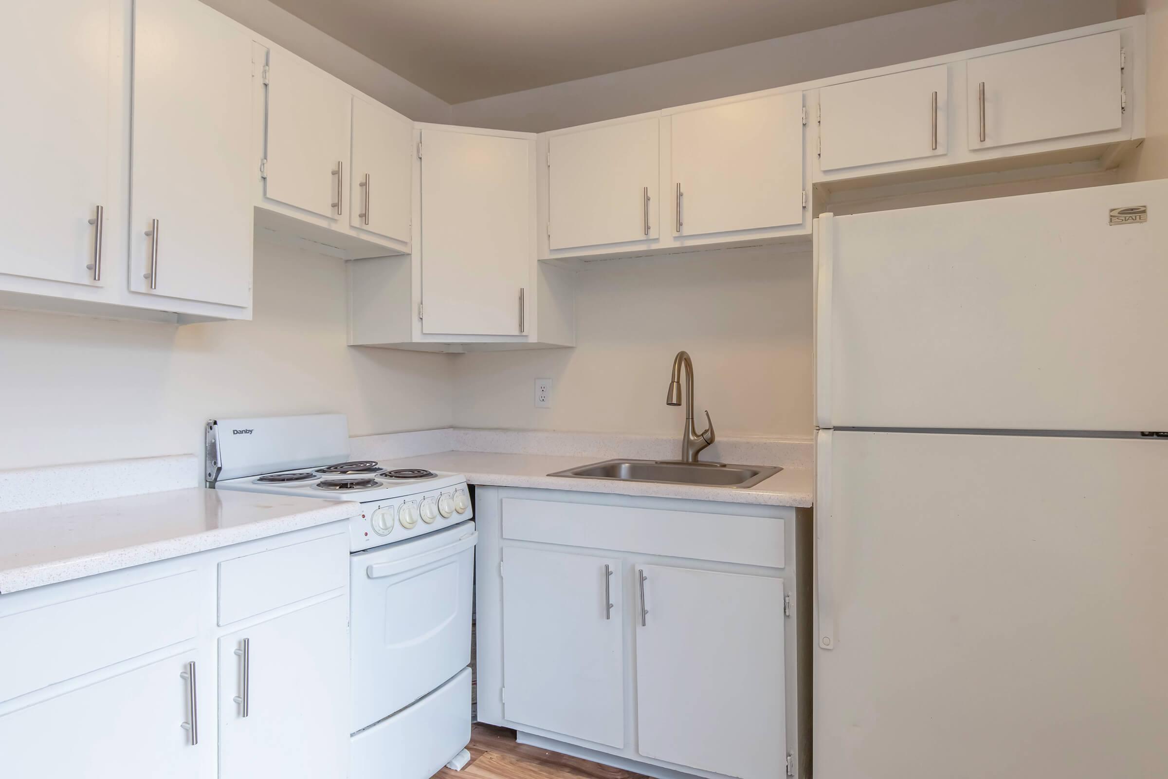 Modern kitchen with white cabinets, a white stove, and a stainless steel sink. The refrigerator is also white, and the countertops are light-colored. The space is well-lit, creating a clean and inviting atmosphere.