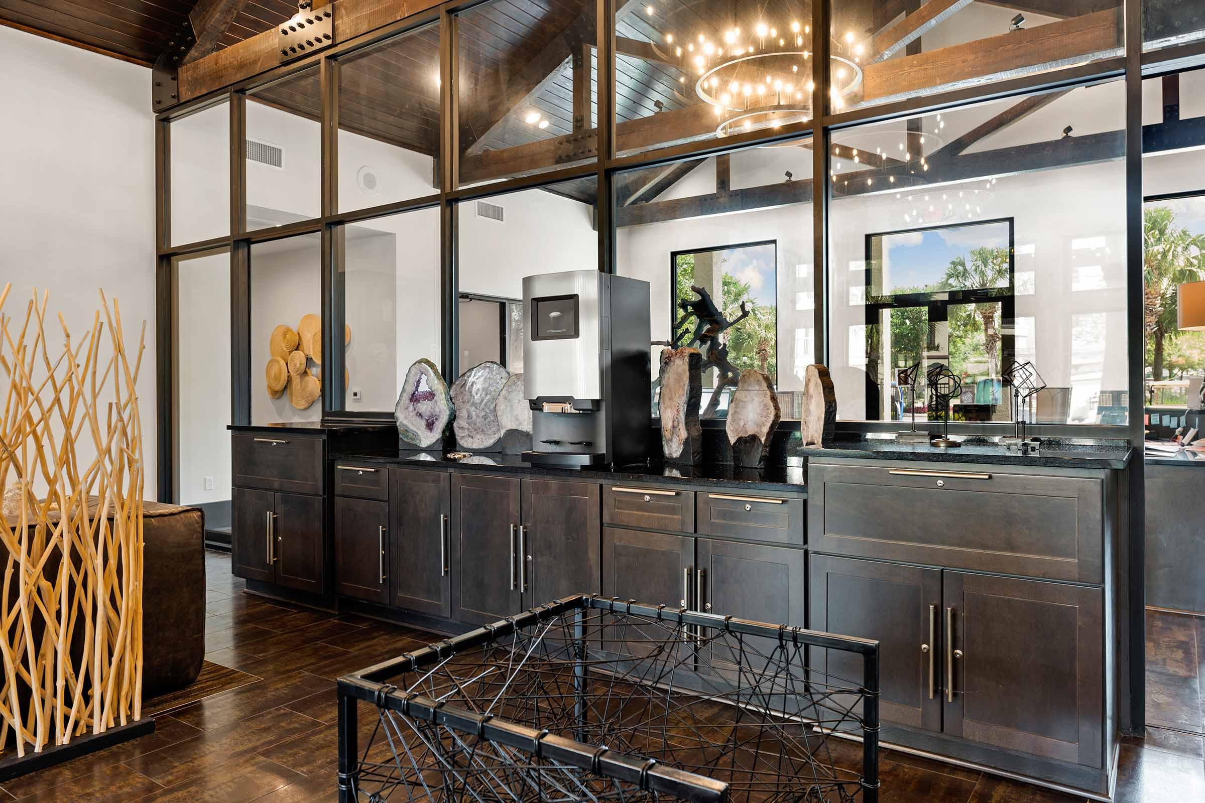 Interior of a modern stylish room featuring a sleek black cabinet with decorative stone sculptures, a large glass window wall, a contemporary chandelier overhead, and artistic wooden elements. The space combines natural textures and modern design for a sophisticated atmosphere.