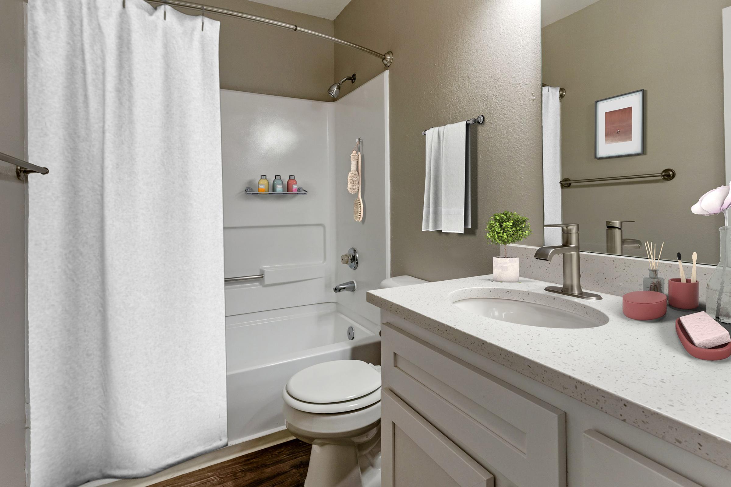 A modern bathroom featuring a white shower curtain, a clean bathtub with shelves containing bottles, and a light-colored countertop with a sink. Decorative elements include a potted plant, towels, and bathroom accessories. The walls are painted in a neutral tone, creating a calming atmosphere.