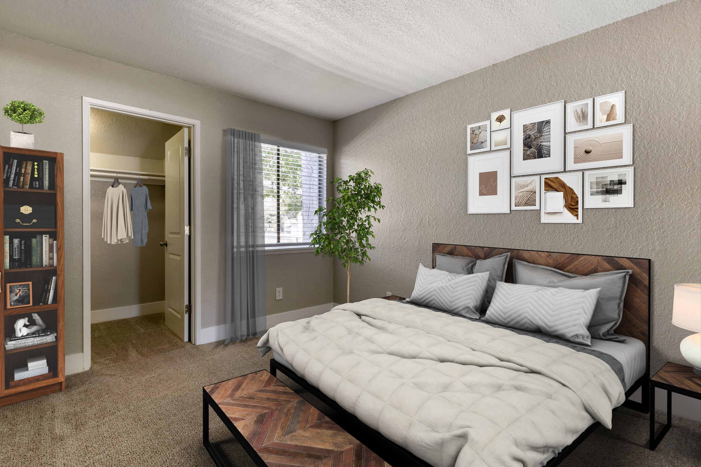 A cozy bedroom featuring a large bed with a light-colored quilt, two bedside tables, and decorative pillows. There’s a bookshelf with books, a plant, and a closet partially visible. The room has a window with sheer curtains, allowing natural light in, and wall art displays above the bed.