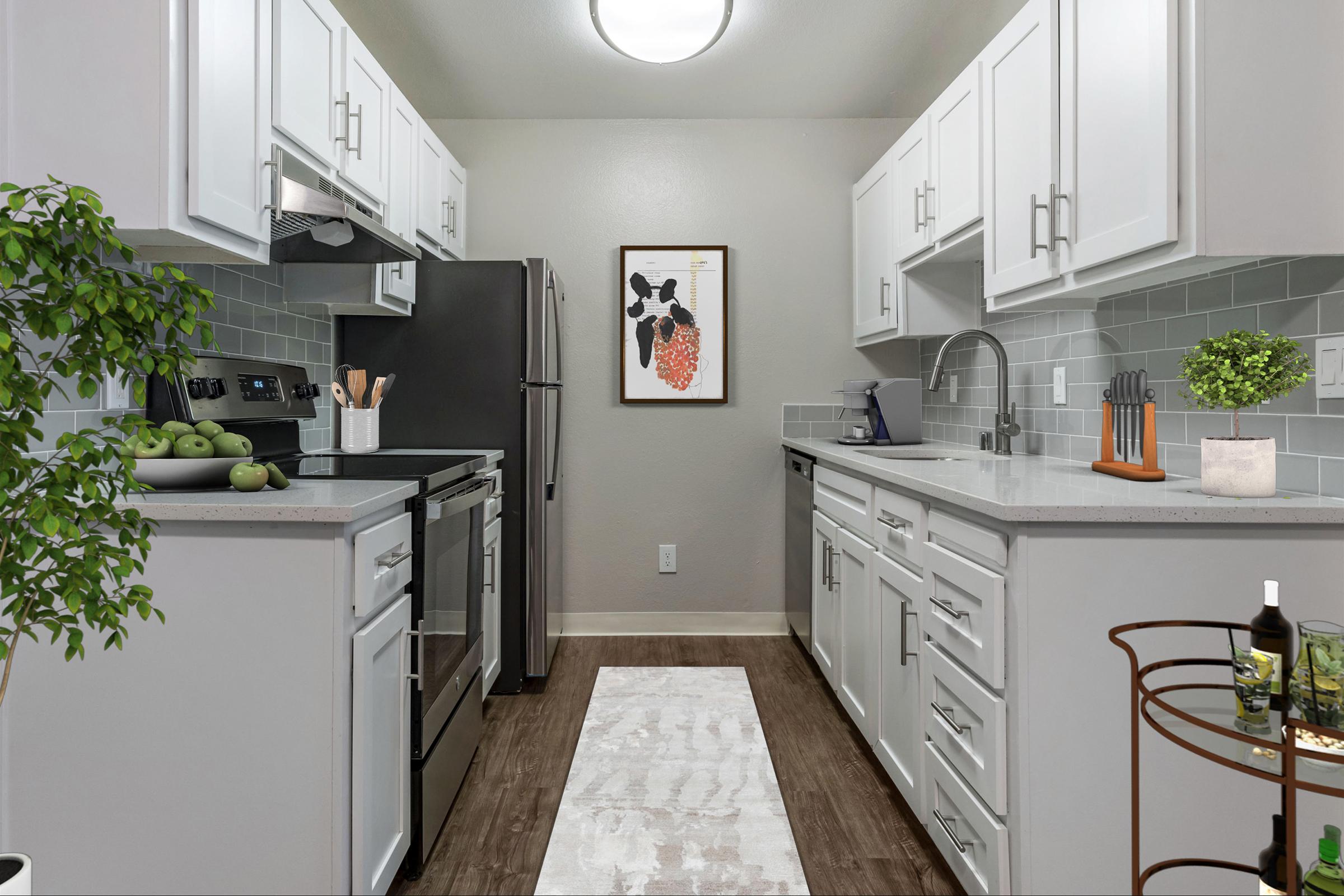 A modern kitchen featuring white cabinets, stainless steel appliances, and a light-colored countertop. A framed artwork hangs on the wall, and a small indoor plant sits on the counter. A runner rug adds warmth, while a wine cart with glasses and a bottle is positioned nearby.