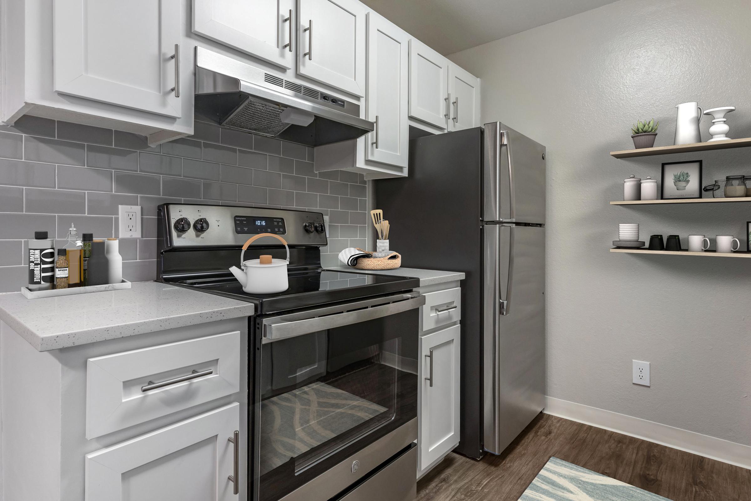 Modern kitchen featuring white cabinetry, stainless steel appliances, including an oven and refrigerator, and a gray-tiled backsplash. A white pot sits on the stove, with kitchen utensils displayed nearby. A minimalist shelf displays small decor items and dishes, enhancing the contemporary aesthetic.