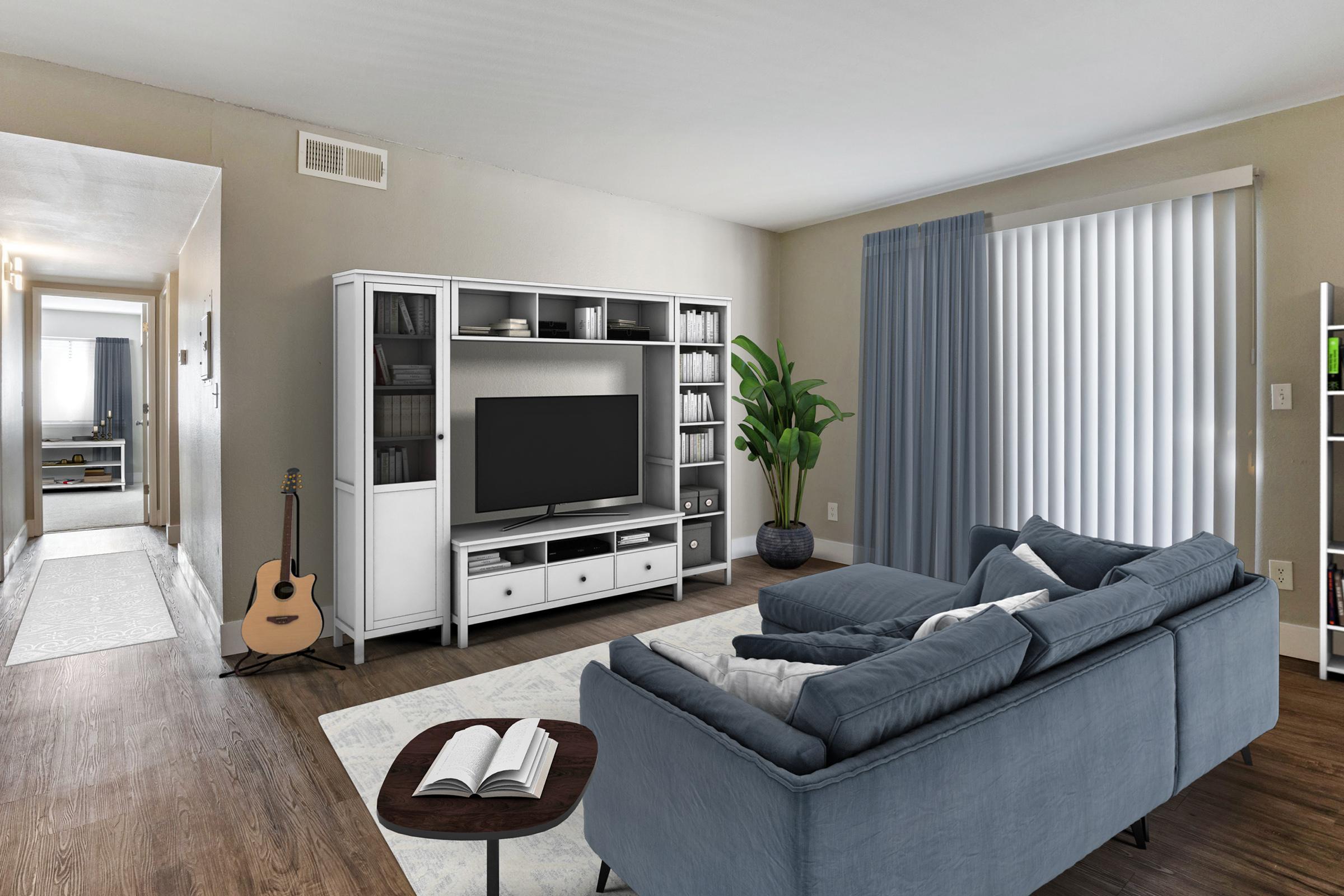 A modern living room featuring a blue sofa, a wooden coffee table with a book, and a white entertainment center with a TV. There’s an acoustic guitar leaning against the wall, and light-colored curtains cover the windows. A hallway can be seen in the background, adding depth to the space.