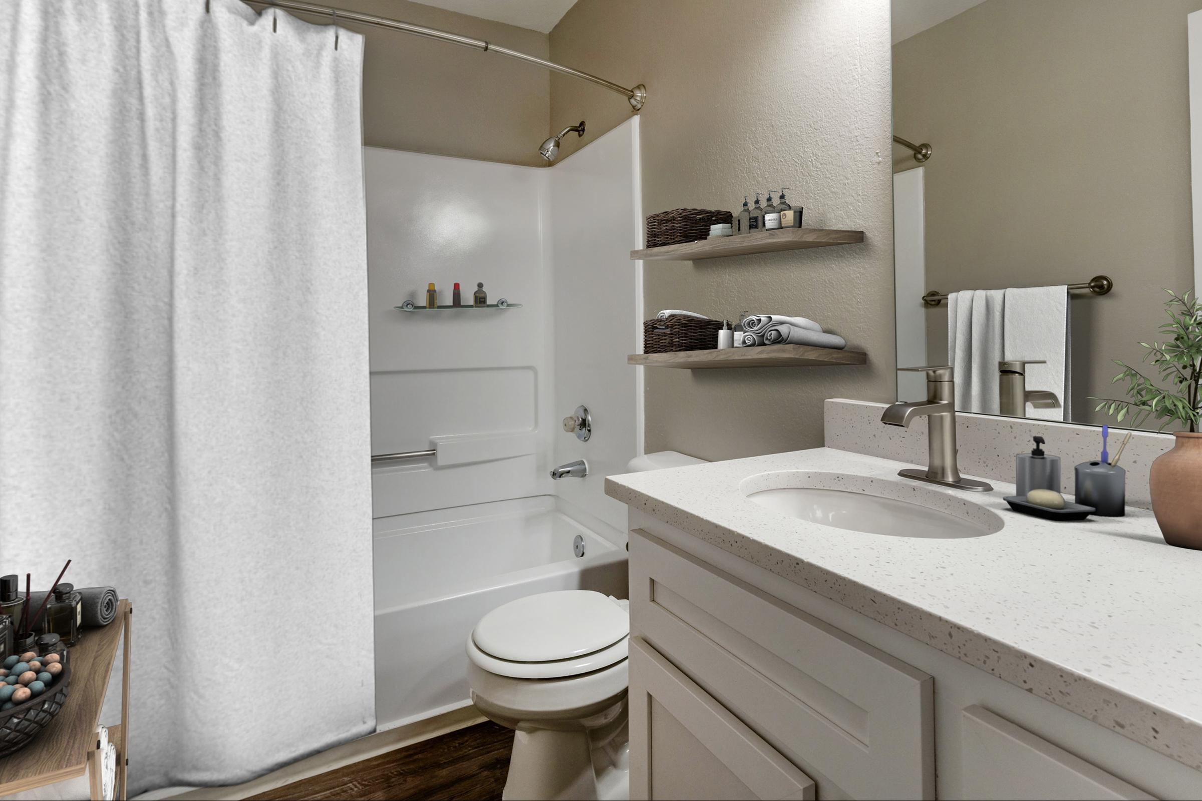 A well-lit bathroom featuring a white shower curtain, a bathtub with shelves holding toiletries, a modern sink with a countertop, and neatly arranged towels. The decor includes natural elements like a small plant and decorative items on the counter, creating a tidy and inviting atmosphere.