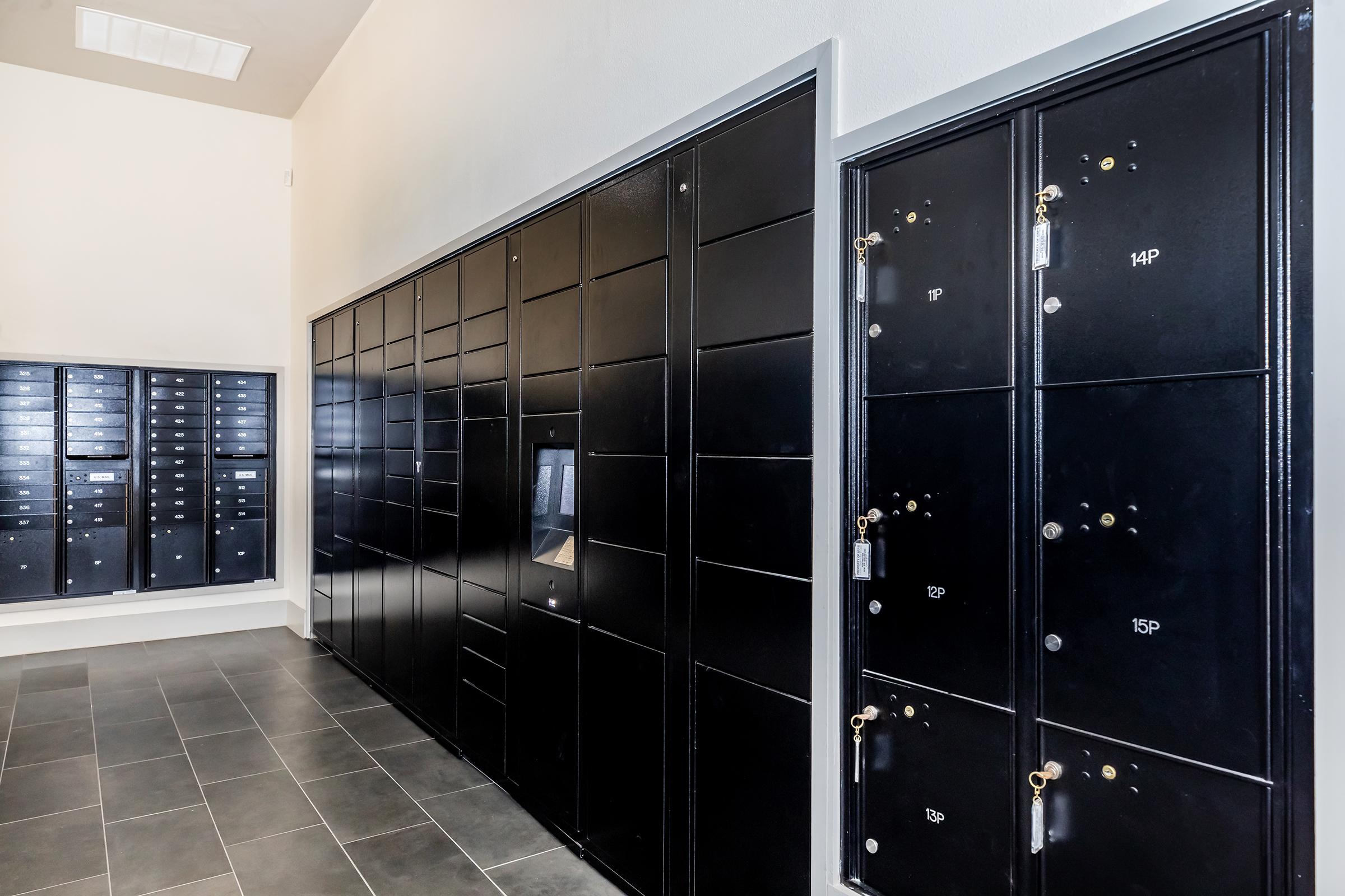 A corridor featuring multiple black mailboxes lined along the walls. The left side showcases a series of smaller mailboxes, while the right side has larger individual compartments, some with keys visible. The floor is tiled, and the walls have a neutral color, creating a clean and organized look.