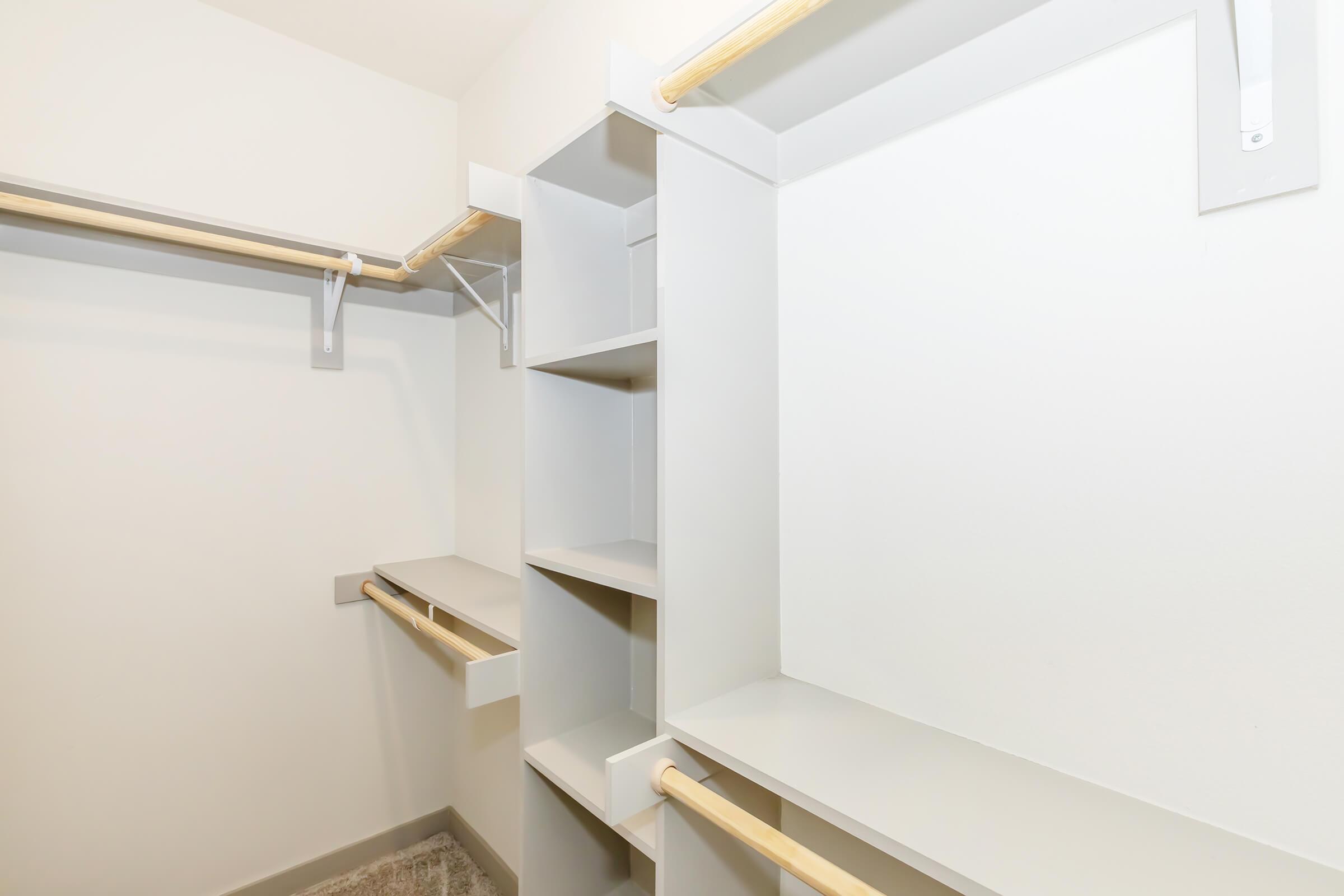 A clean, empty closet featuring built-in shelves and two hanging rods. The walls are painted a light color, creating a bright and spacious appearance. The floor is carpeted, and the overall design is modern and minimalistic.