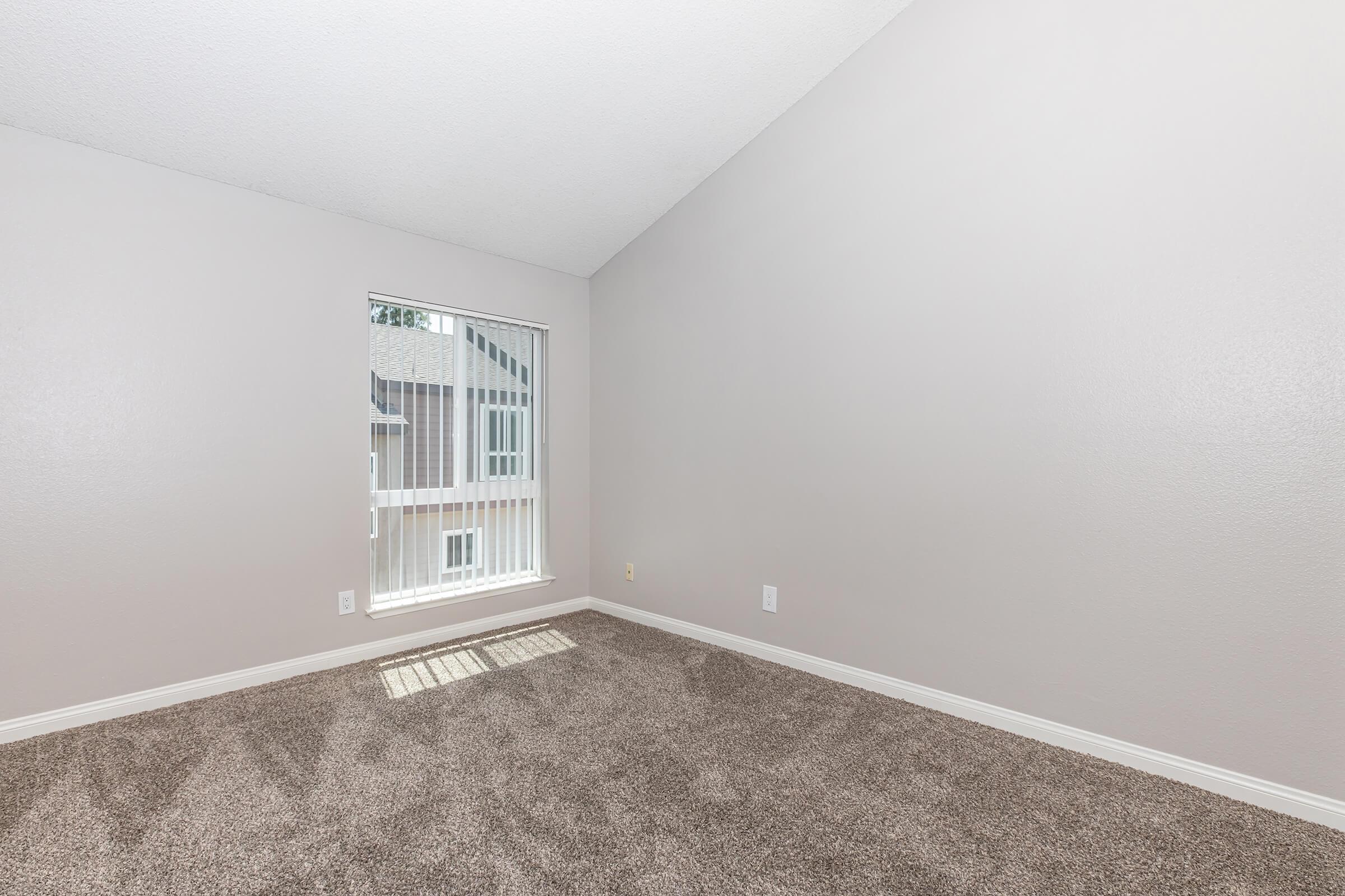 High-end Apartments in Riverside CA - Canyon Crest Views - Spacious Carpeted Bedroom With Light Gray Walls, Large Window With Vertical Blinds, And Natural Daylight