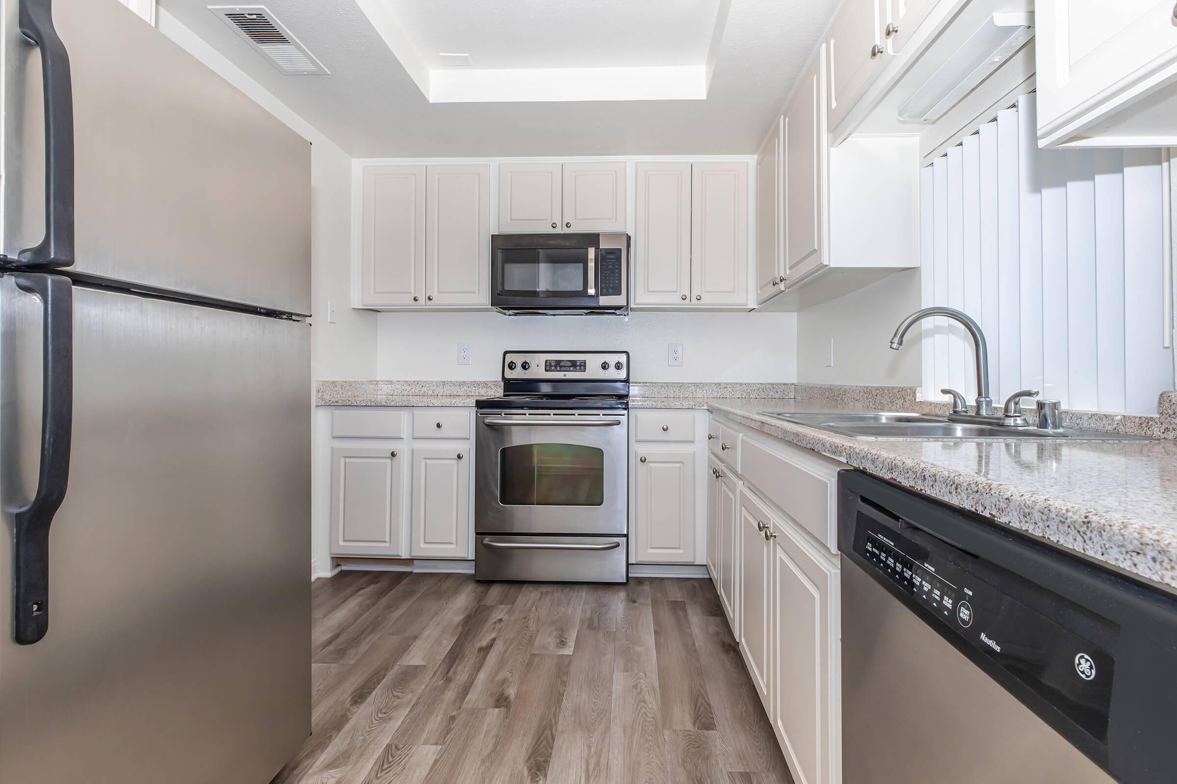 2 Bedroom luxury Apartments in Riverside CA - Canyon Crest Views - Bright White Kitchen With Granite Counters, Stainless Steel Appliances, Double Sink, and Wood Style Flooring