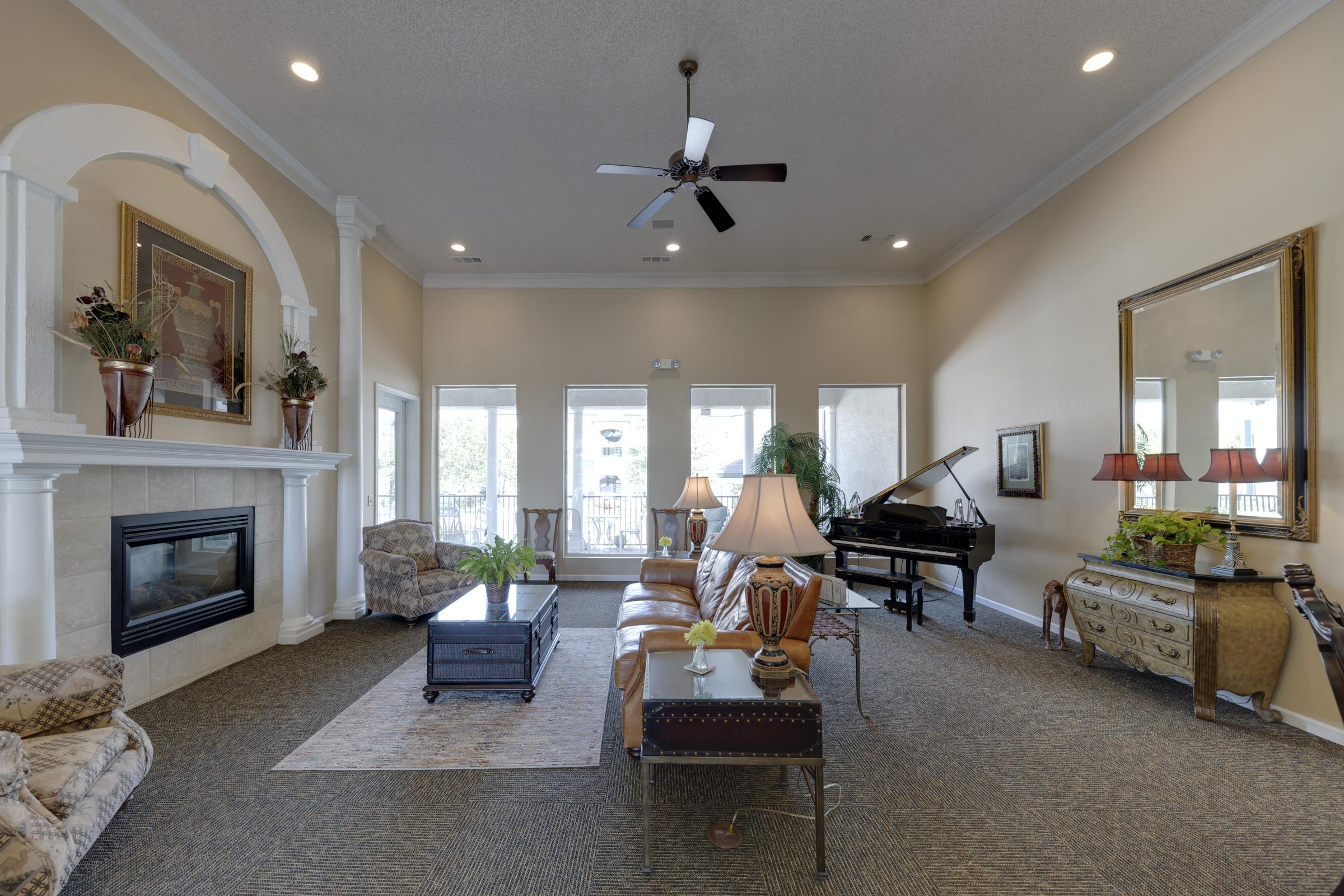 Spacious living room featuring a fireplace, large windows, and elegant decor. There are comfortable leather couches, a piano, and decorative plants, along with a coffee table and an antique chest. The walls are painted in warm tones, complemented by stylish lighting fixtures.
