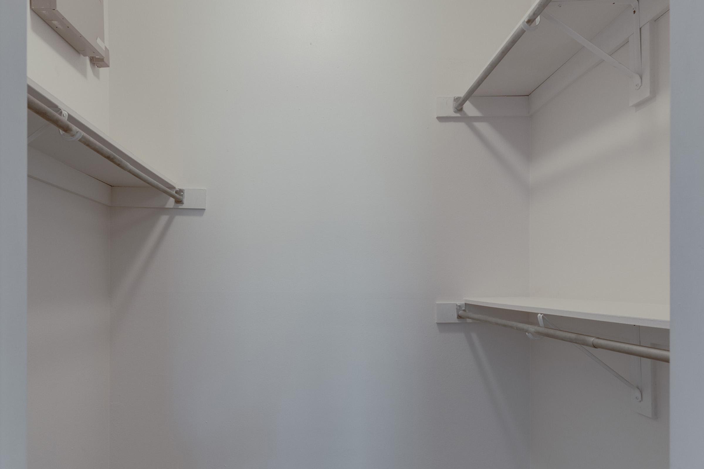 Empty closet with white walls and two horizontal shelves on opposite sides, one high and one low, creating a minimalistic and clean look.