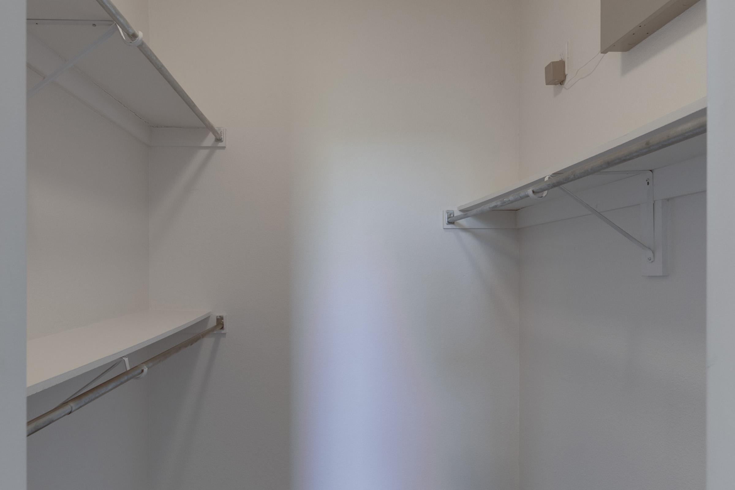 Empty closet with white walls and two shelves on opposite sides. The space is well-lit, showing a simple and clean design, ideal for organization.