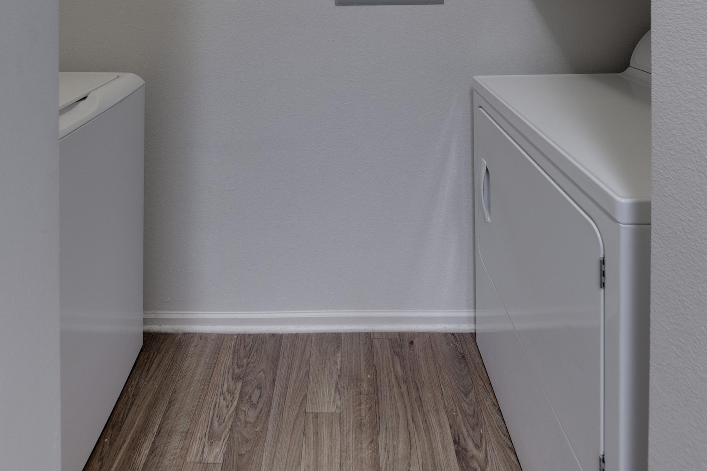 A laundry room featuring a washing machine on the left and a dryer on the right, with light-colored walls and wooden flooring. The space is clean and organized, providing a functional area for laundry tasks.