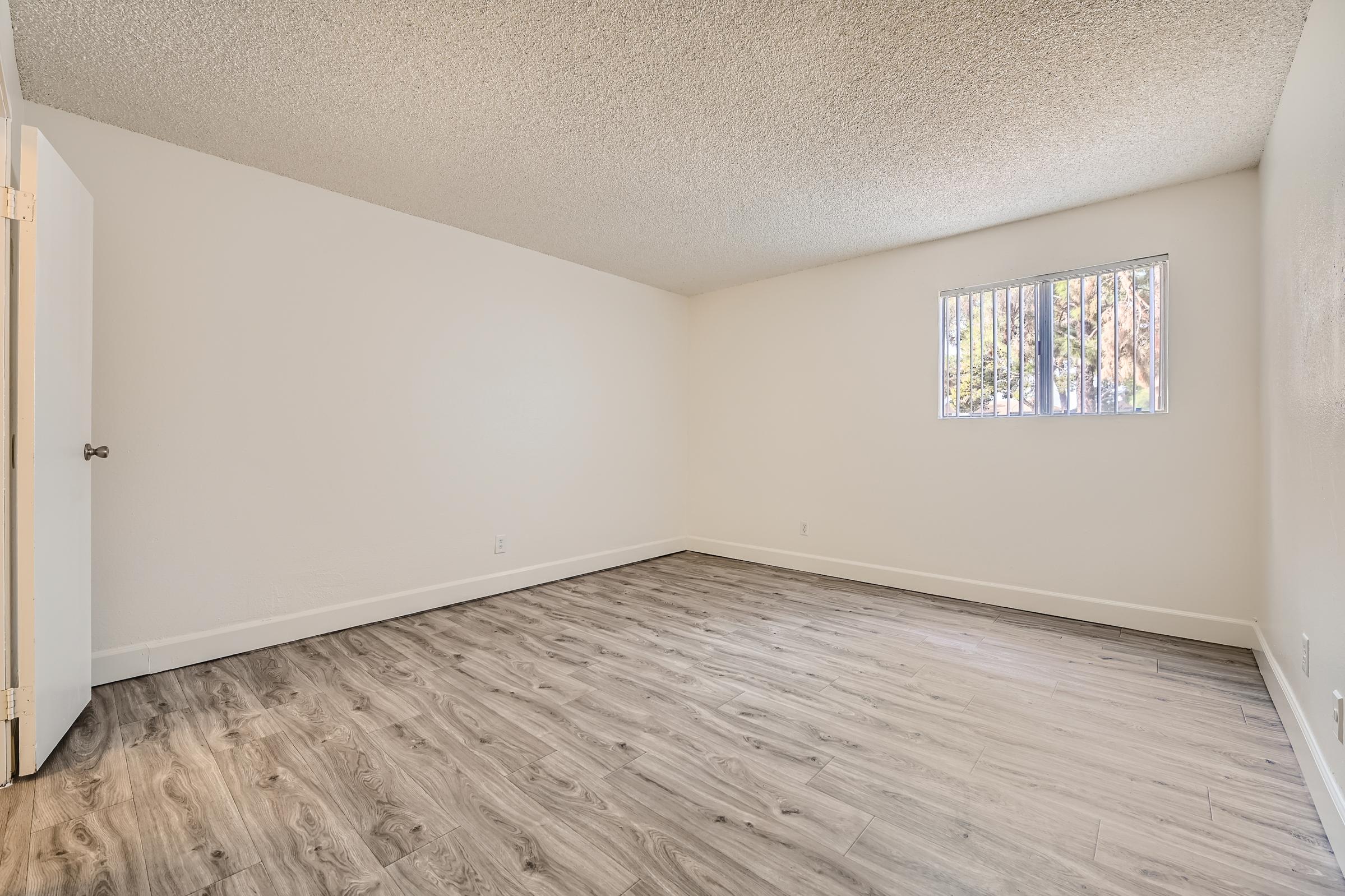 Spacious white bedroom with wooden floors and a window at Rise at the District apartments