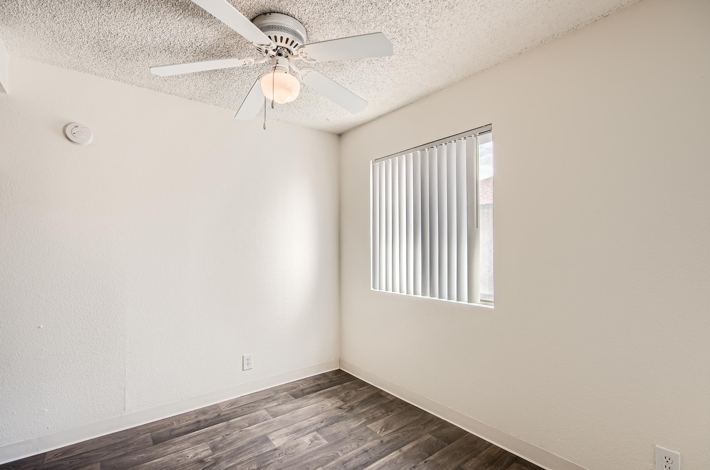 Corner view of an empty Mesa apartment bedroom with a window and ceiling fan