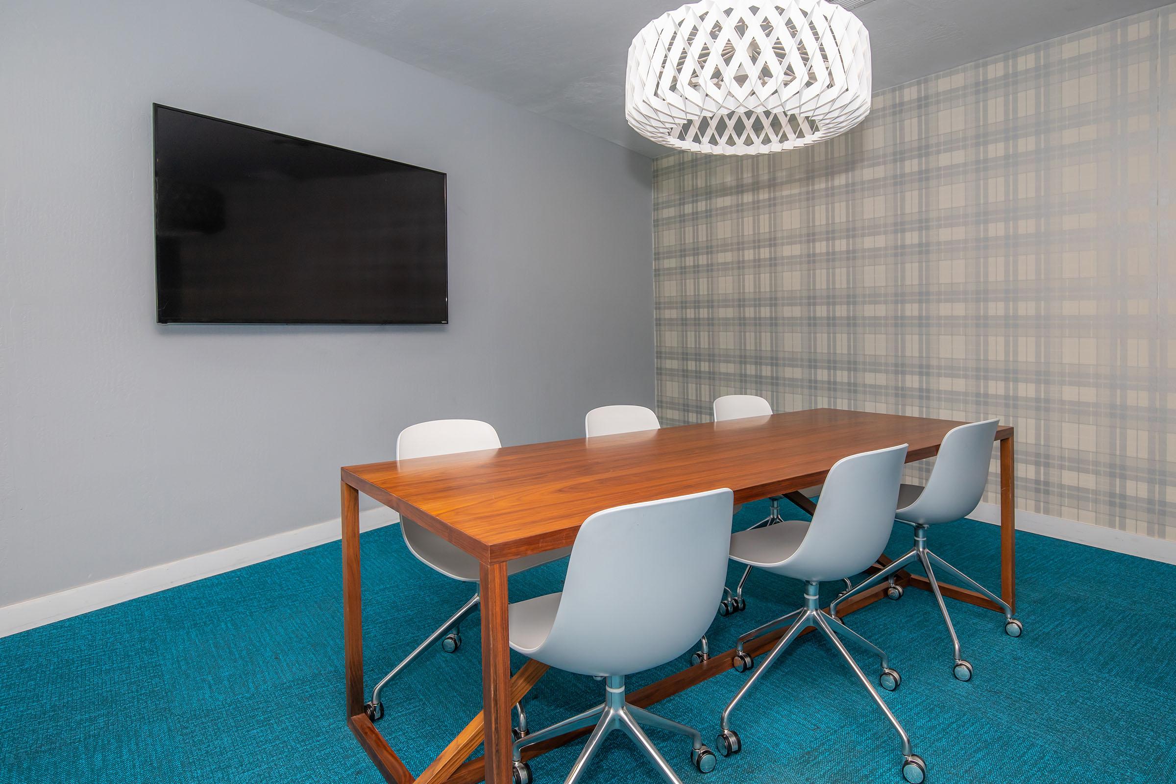 Community conference room with blue carpeting, large wooden table, rolling chairs, and flat screen TV
